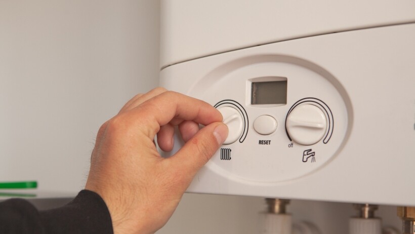 Electric boiler vs gas boiler -  A close-up of a person adjusting the control knob on a white gas boiler