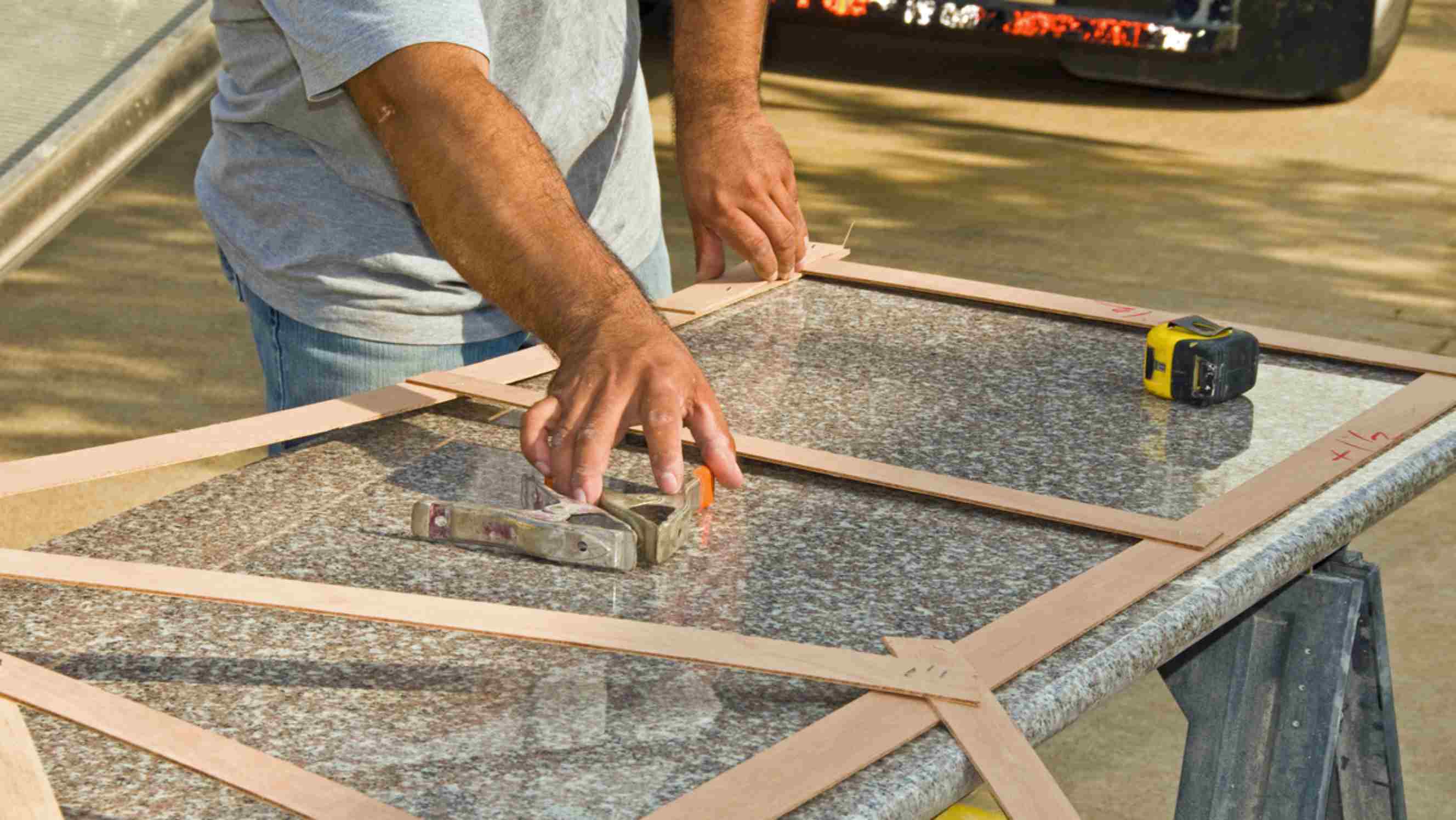 Quartz vs granite benchtops - A worker aligning a granite benchtop with measuring tools and wooden guides on a workbench outdoors