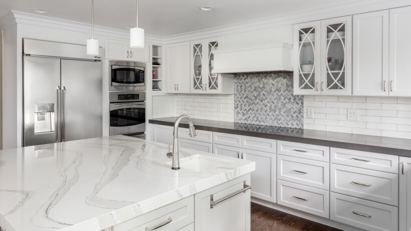 Quartz vs granite benchtops - A modern kitchen featuring a polished white quartz benchtop with subtle grey veining, complemented by white cabinetry and a stainless steel refrigerator