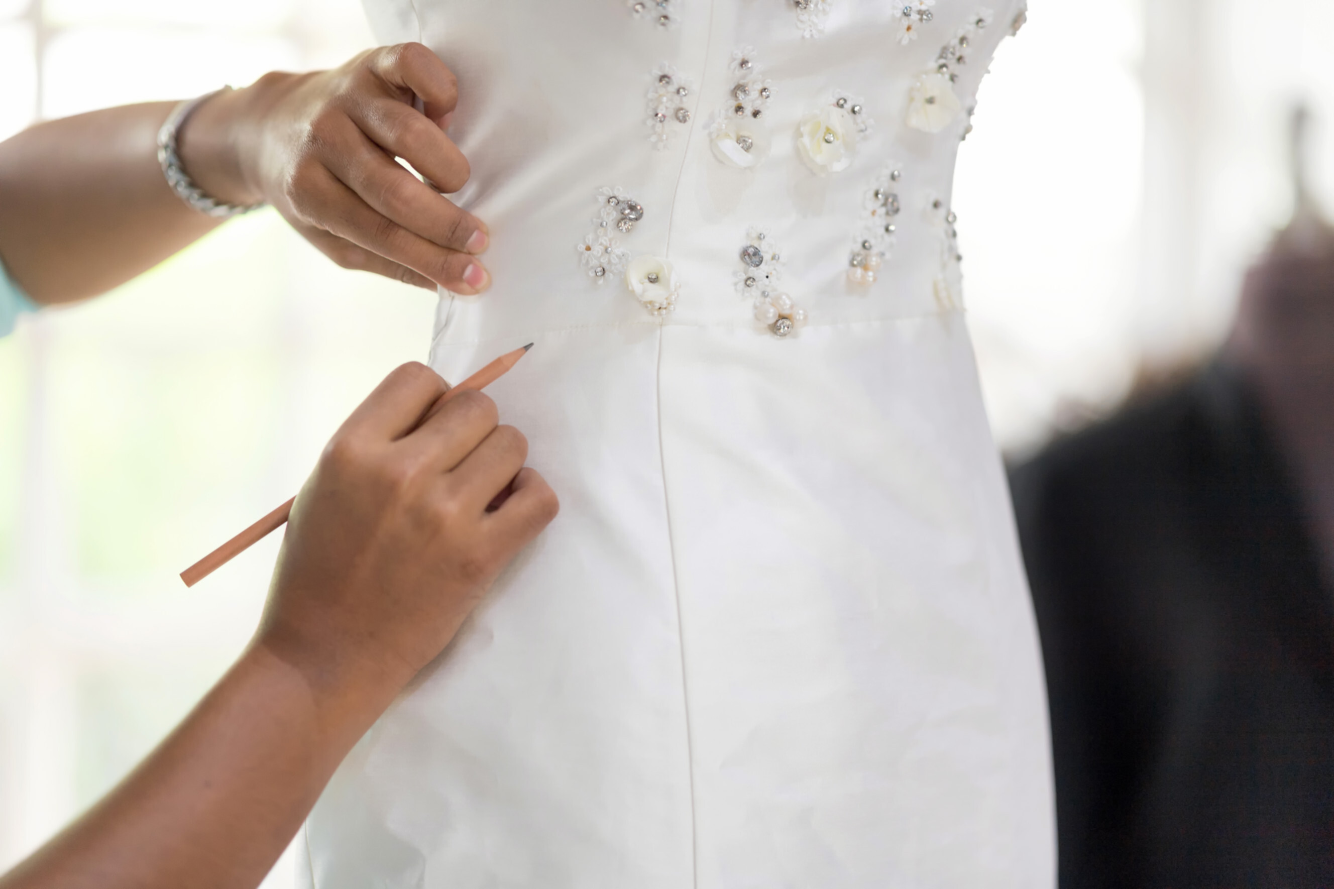 Experienced dressmaker marking adjustments on a detailed white gown, highlighting professional dressmakers near you.