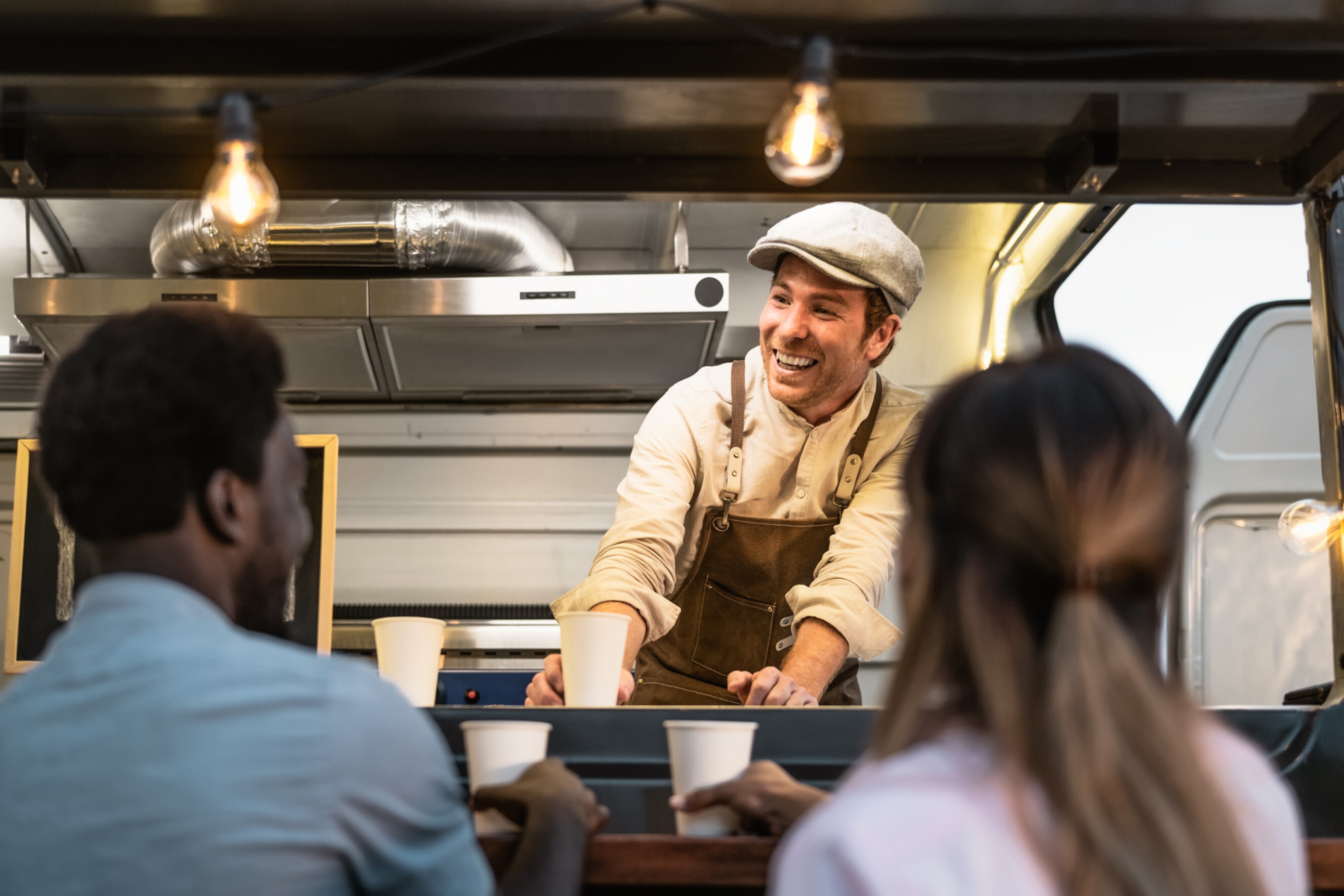 Smiling coffee caterer serving beverages from a food truck to happy customers, highlighting professional coffee catering services near you.