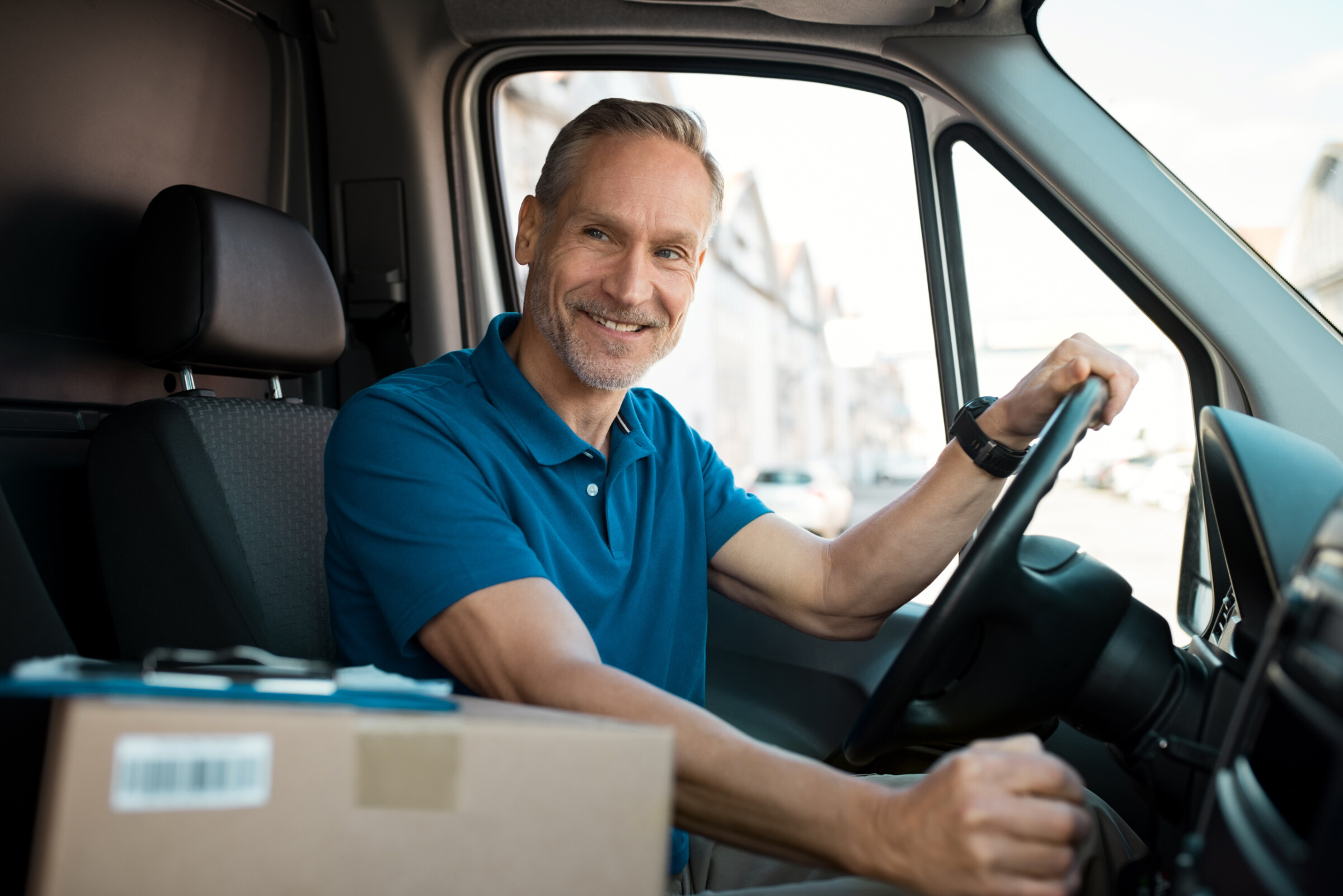 Delivery man driving van with packages on the front seat.