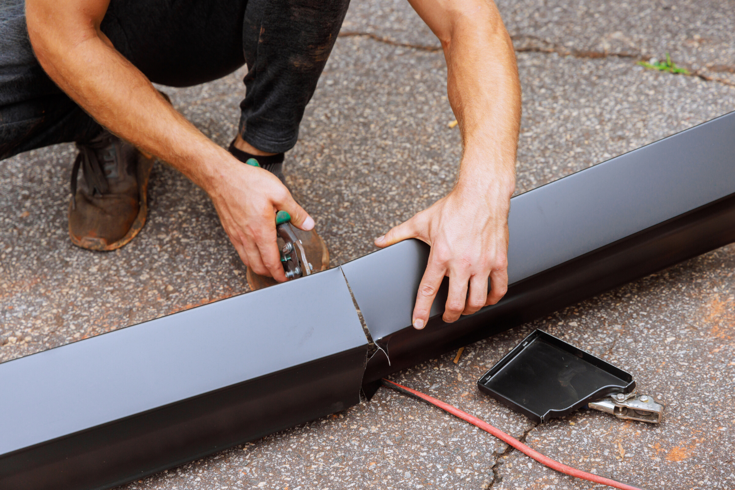 When aluminum rain gutters have been bent on machine tool, worker cuts them to required size with shears