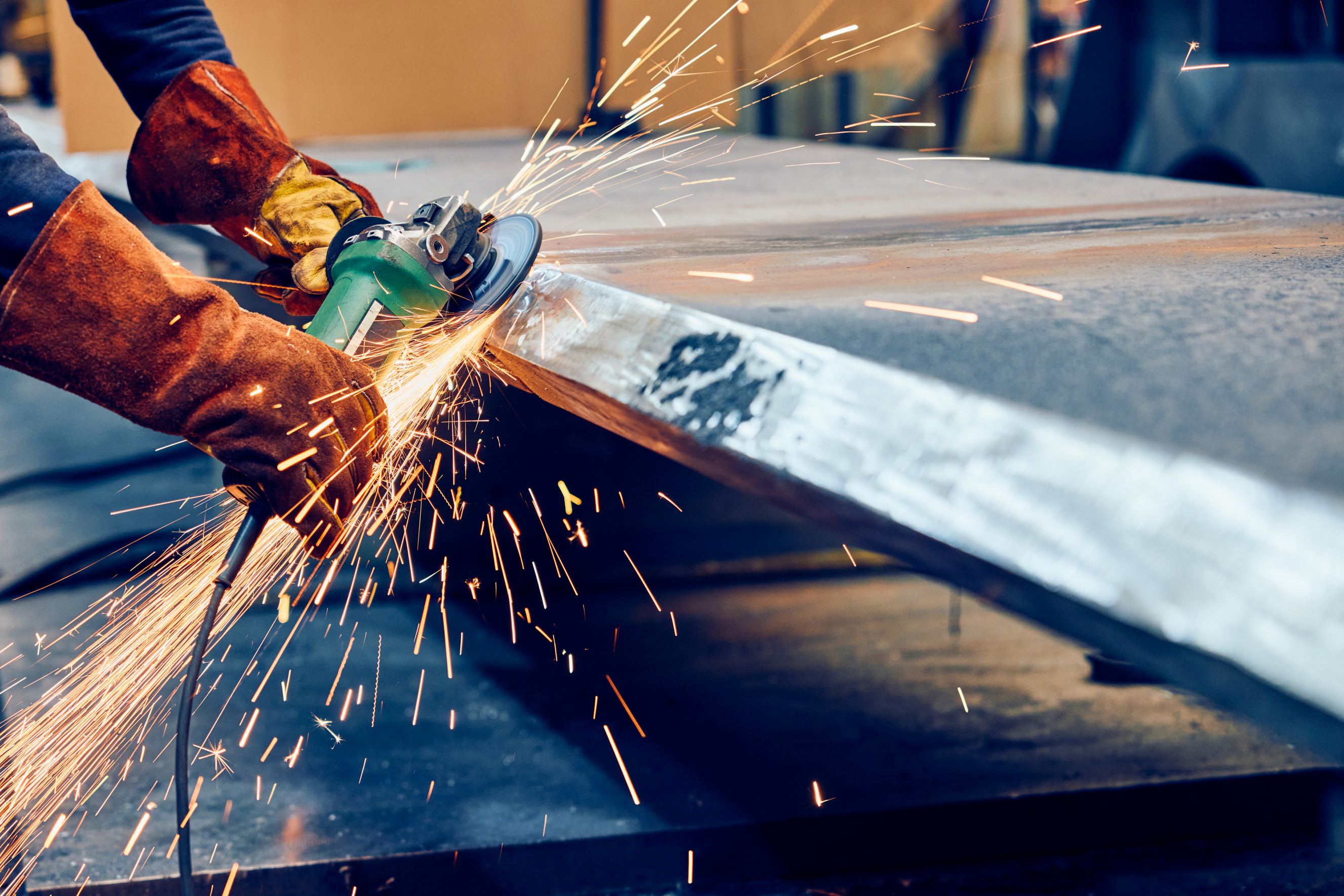 Industrial worker grinding metal surface with angle grinder for metal fabrication.