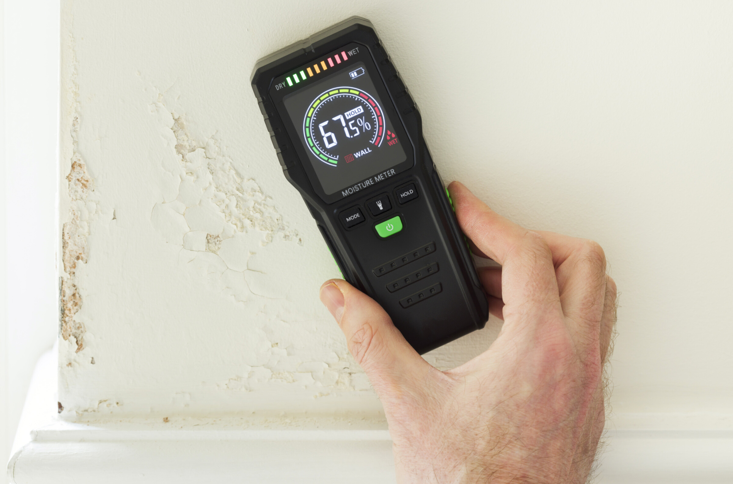 Moisture detector (moisture testing meter) against a wall with rising damp, reading high moisture content.