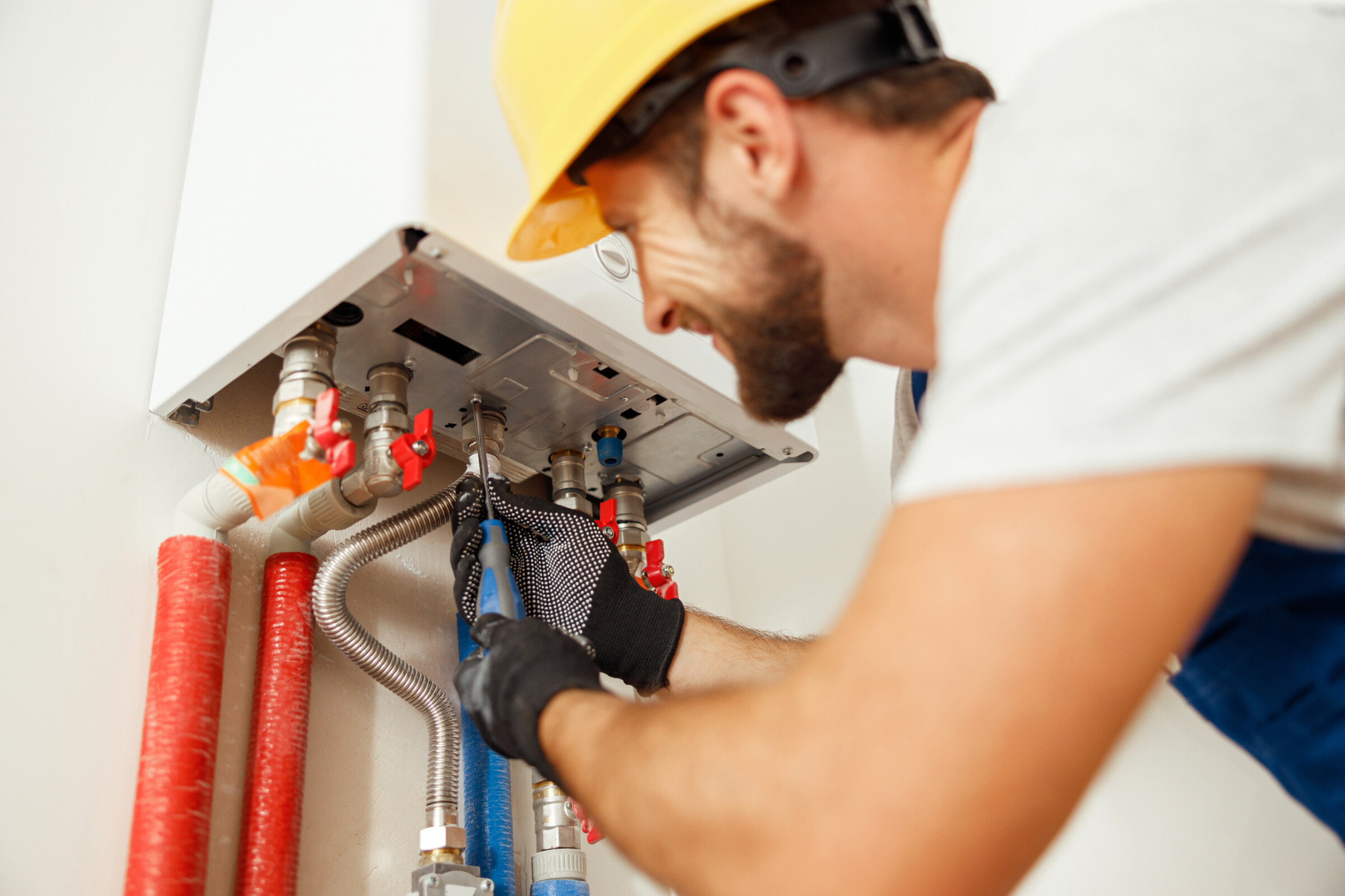 Closeup of plumber using screwdriver while fixing boiler or water heater, working on heating system in apartment