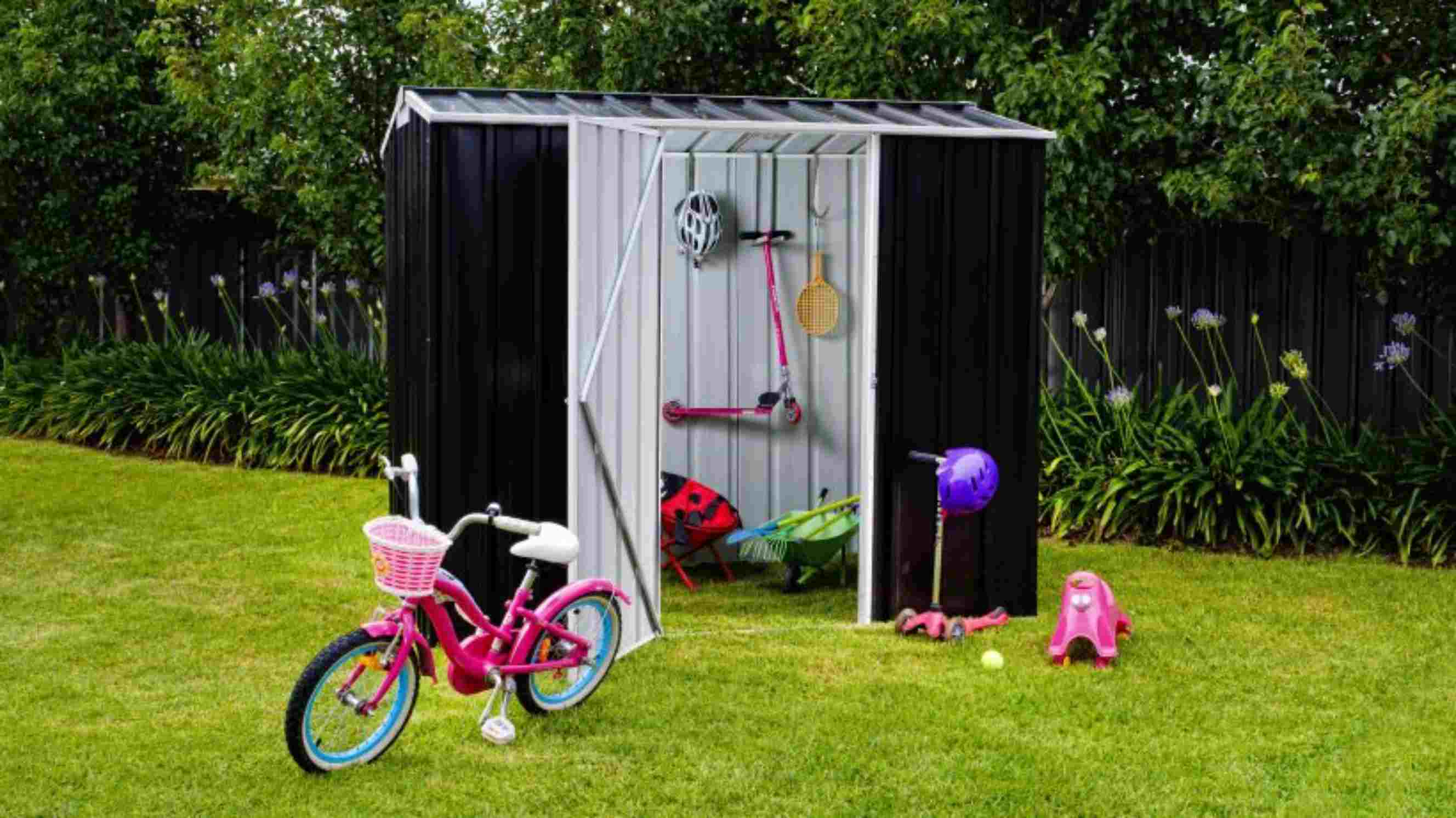 How to insulate a shed - A small black and grey outdoor shed by Easyshed with its door open, showcasing neatly stored items such as a scooter, a bike helmet, a racket, and a wheelbarrow inside.