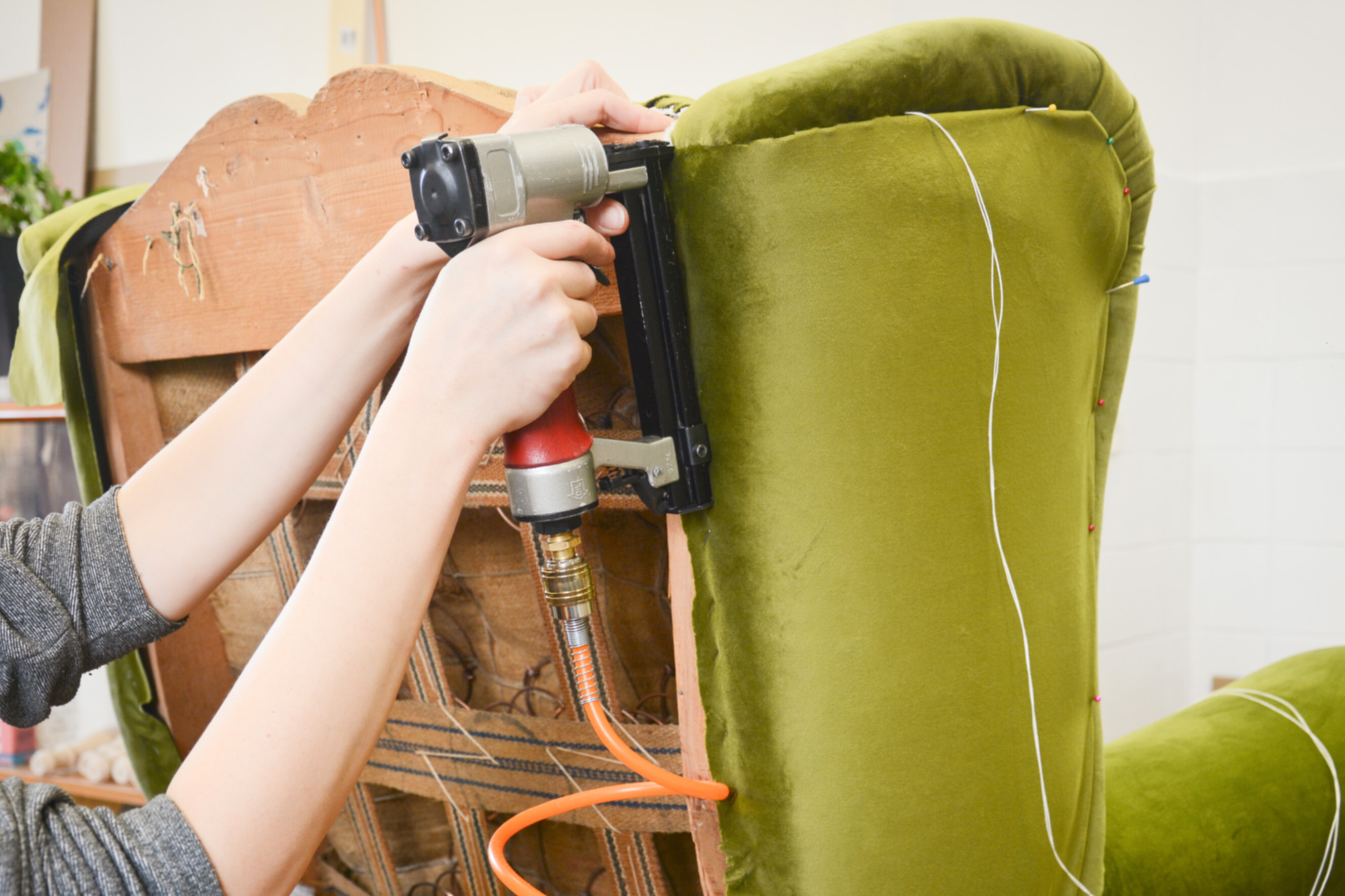 Experienced recliner repair specialist restoring a green upholstered chair with a pneumatic stapler, highlighting highly rated recliner repair services near you.