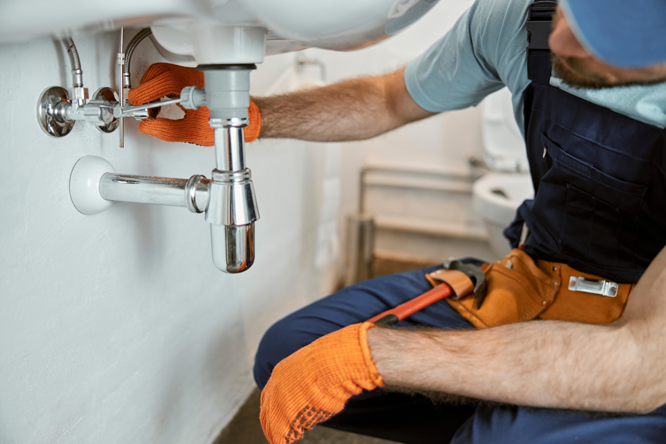 Skilled sink installer tightening connections under a bathroom sink, highlighting expert sink installation services near you.