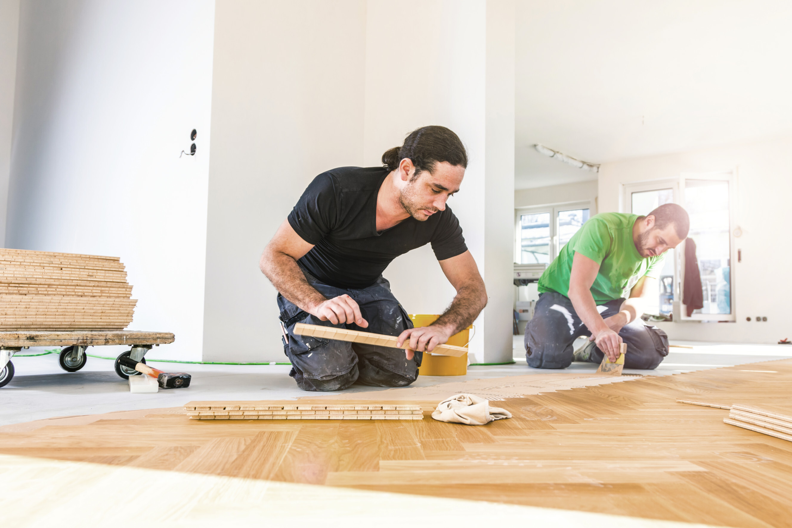 Two professionals installing wooden floorboards in a bright, modern space, highlighting expert floorboard installation and repair services near you.