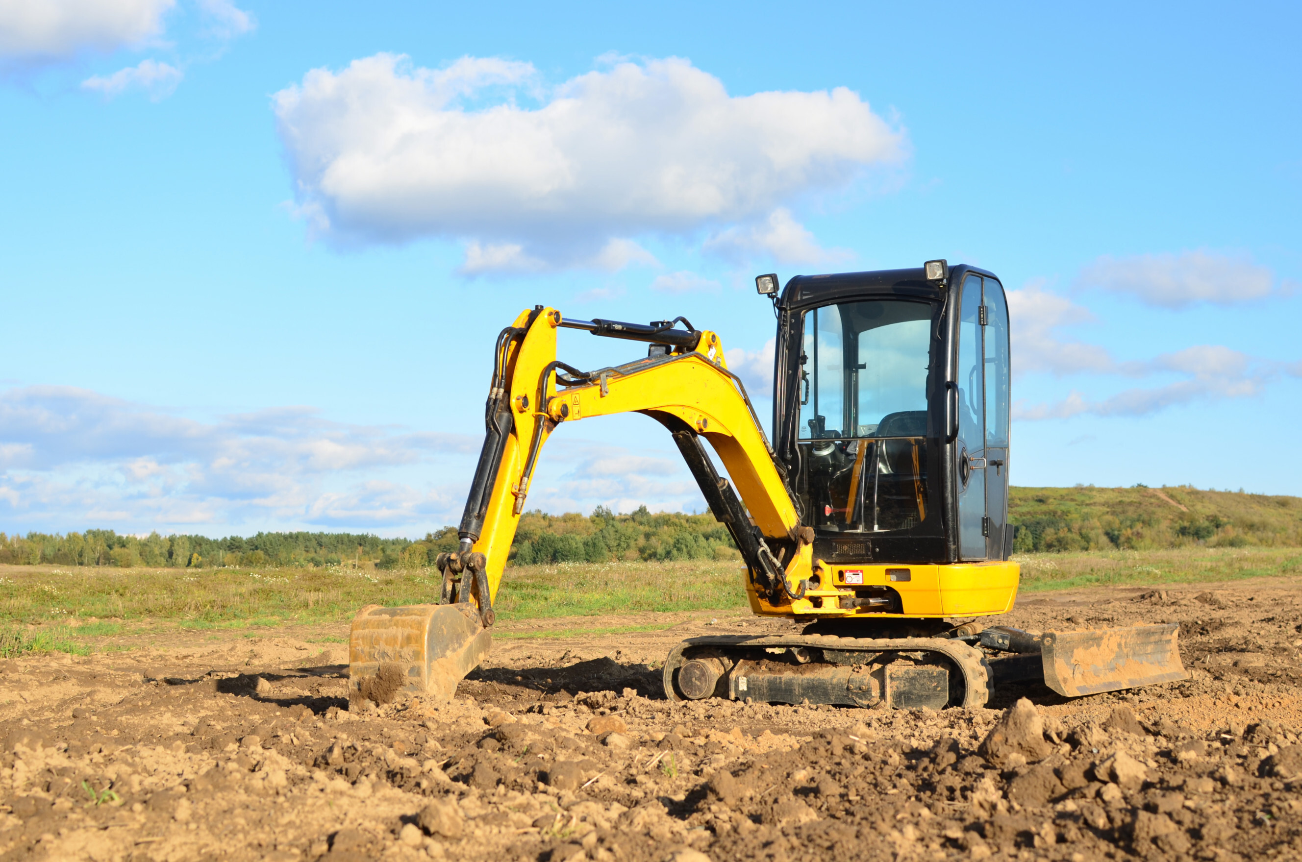 A yellow mini excavator on a construction site, actively digging and moving soil, representing professional earthmoving contractor services near you.