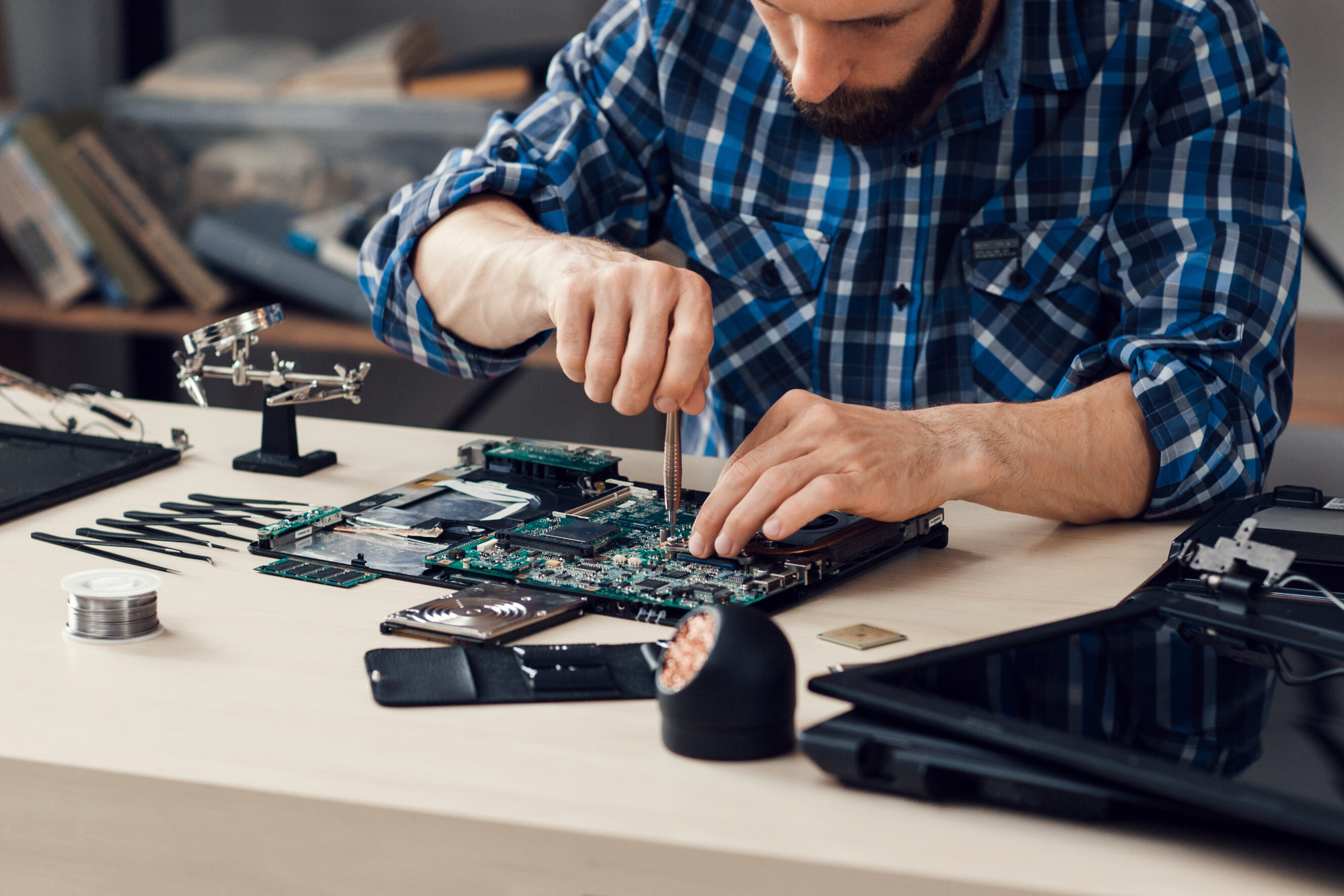 Skilled electronics repair technician working on a disassembled laptop motherboard with precision tools, representing expert electronics repair services near you.