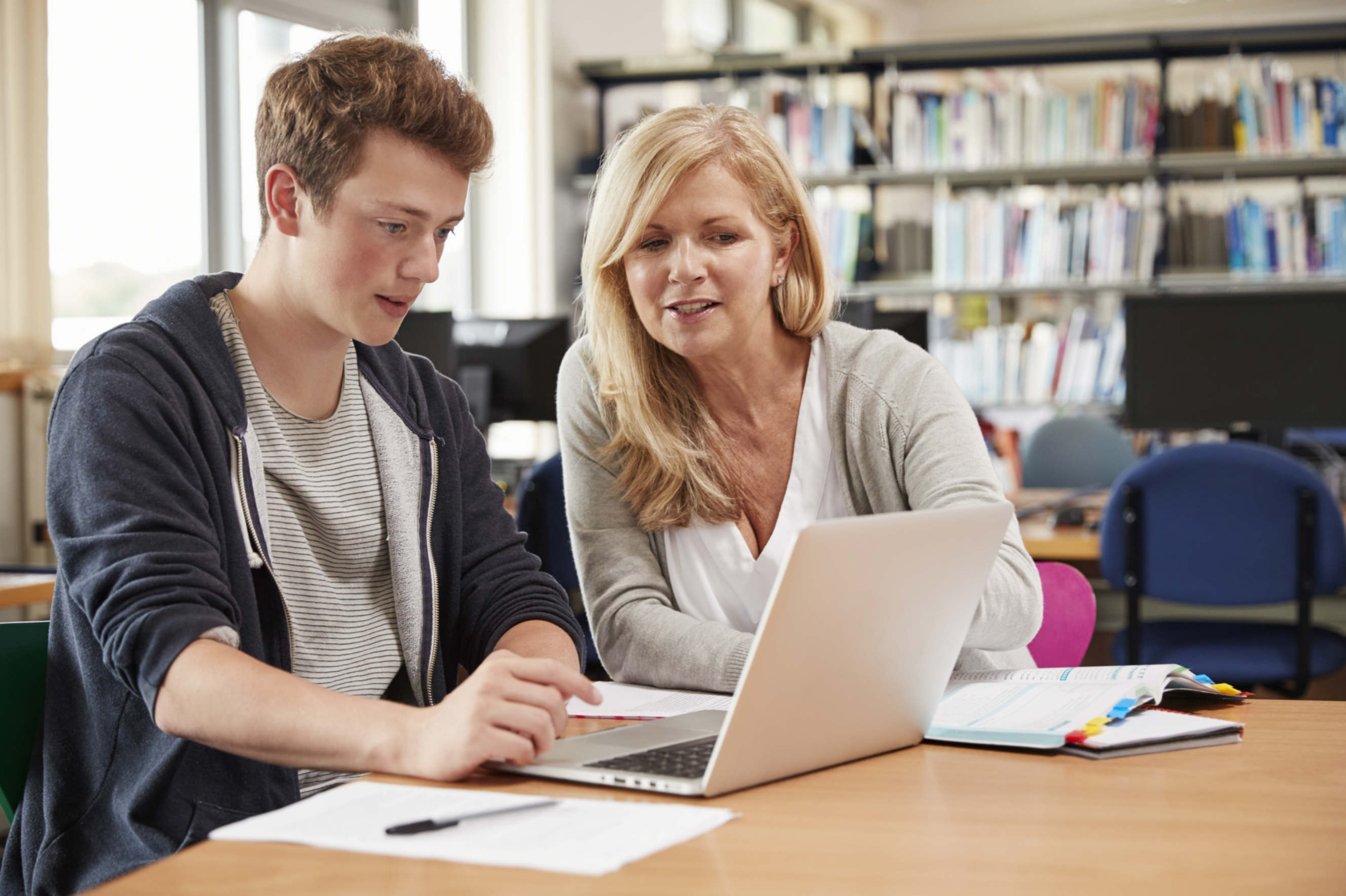 Tutor assisting a student with accounting homework on a laptop in a library.