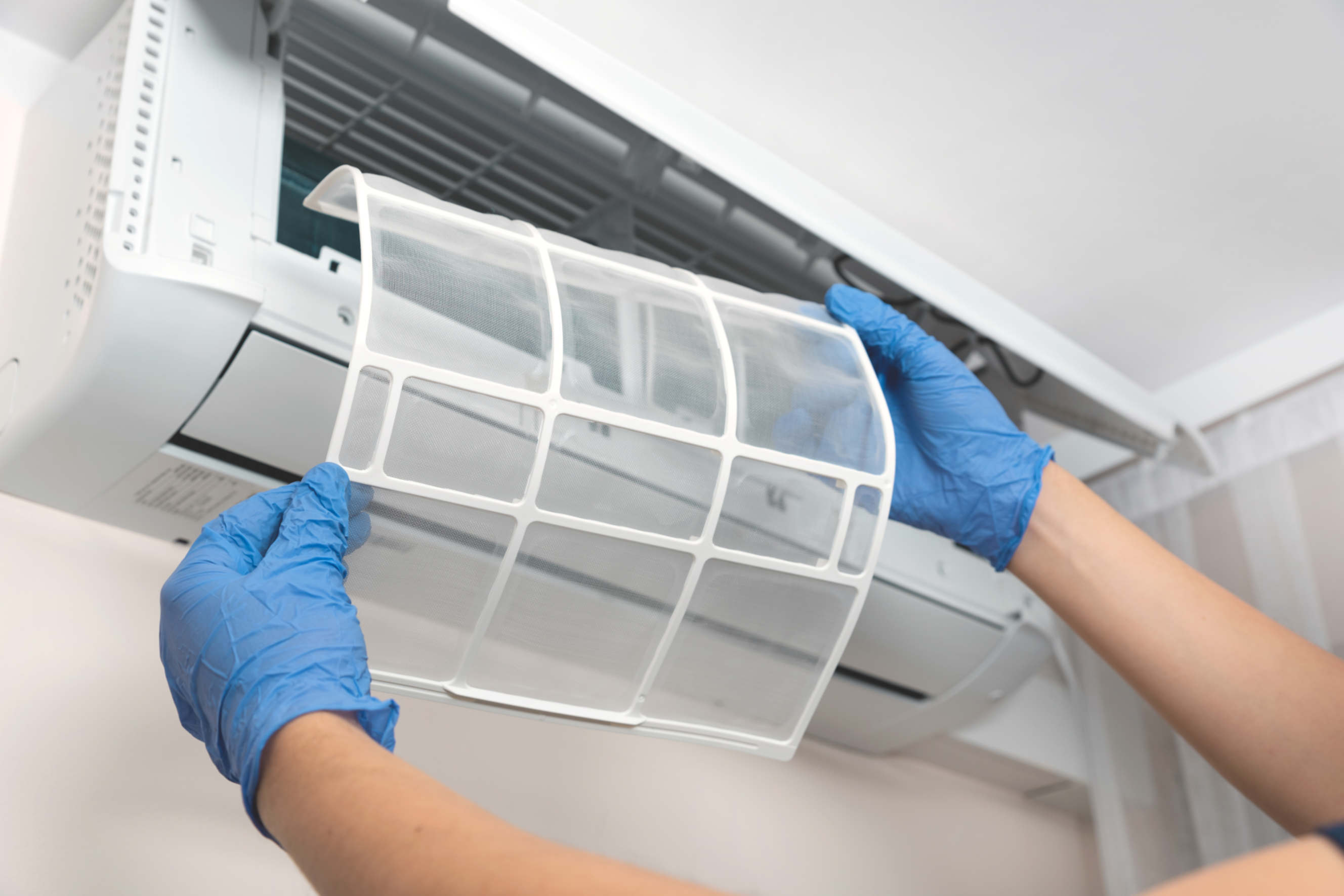 Technician replacing an air conditioner filter while wearing protective gloves.