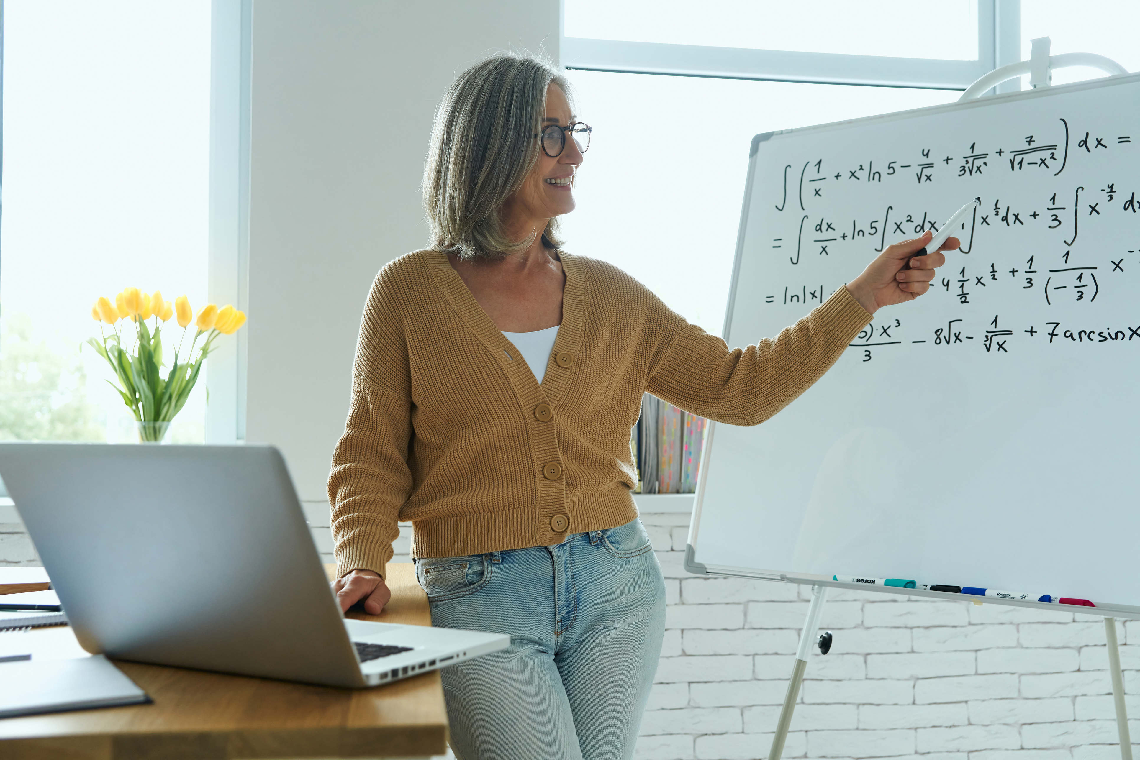 Math tutor explaining algebra equations on a whiteboard in a bright classroom.