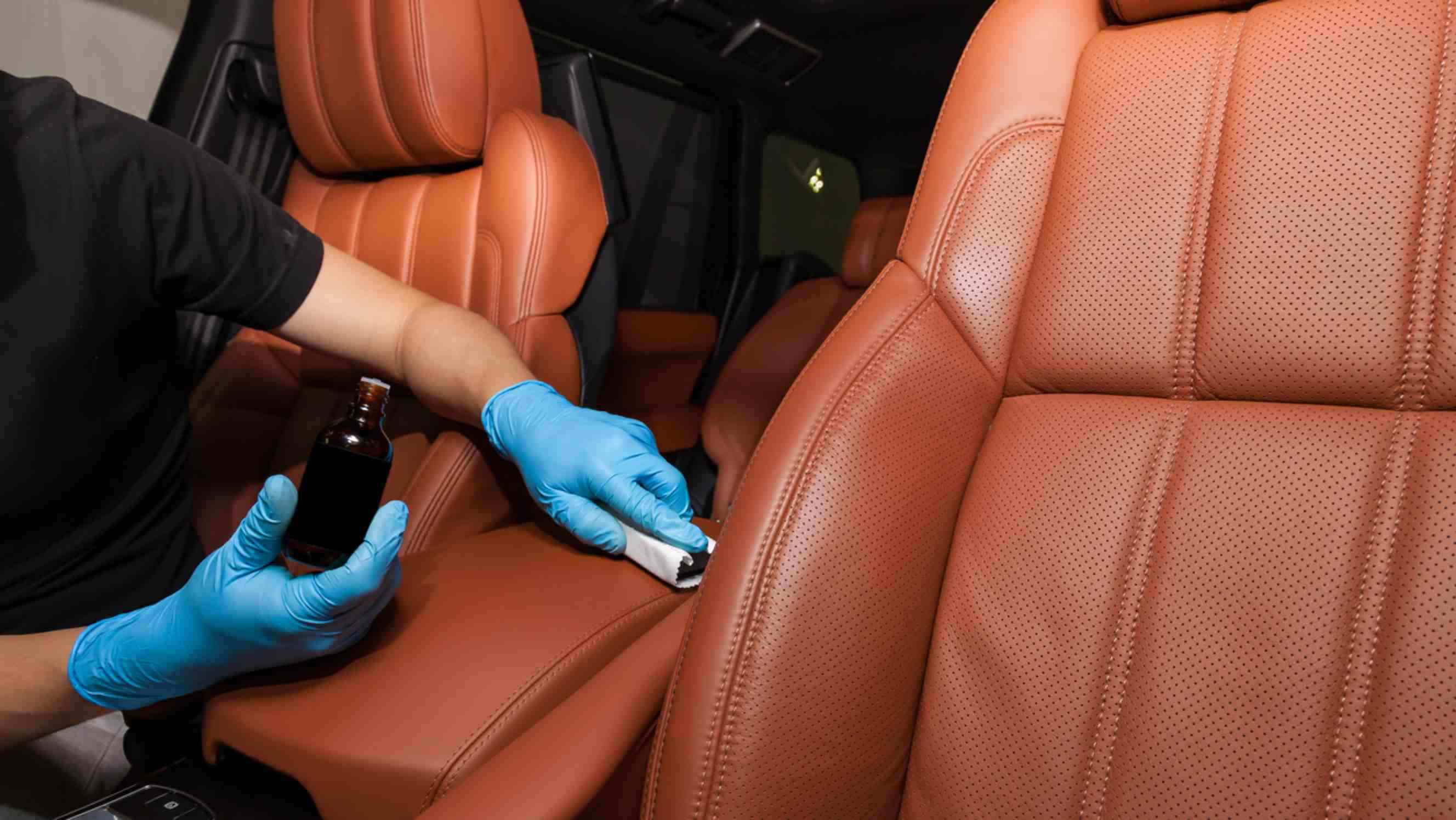 A technician wearing blue gloves carefully restoring tan leather car upholstery using specialised tools, representing professional car upholstery repair services near you.