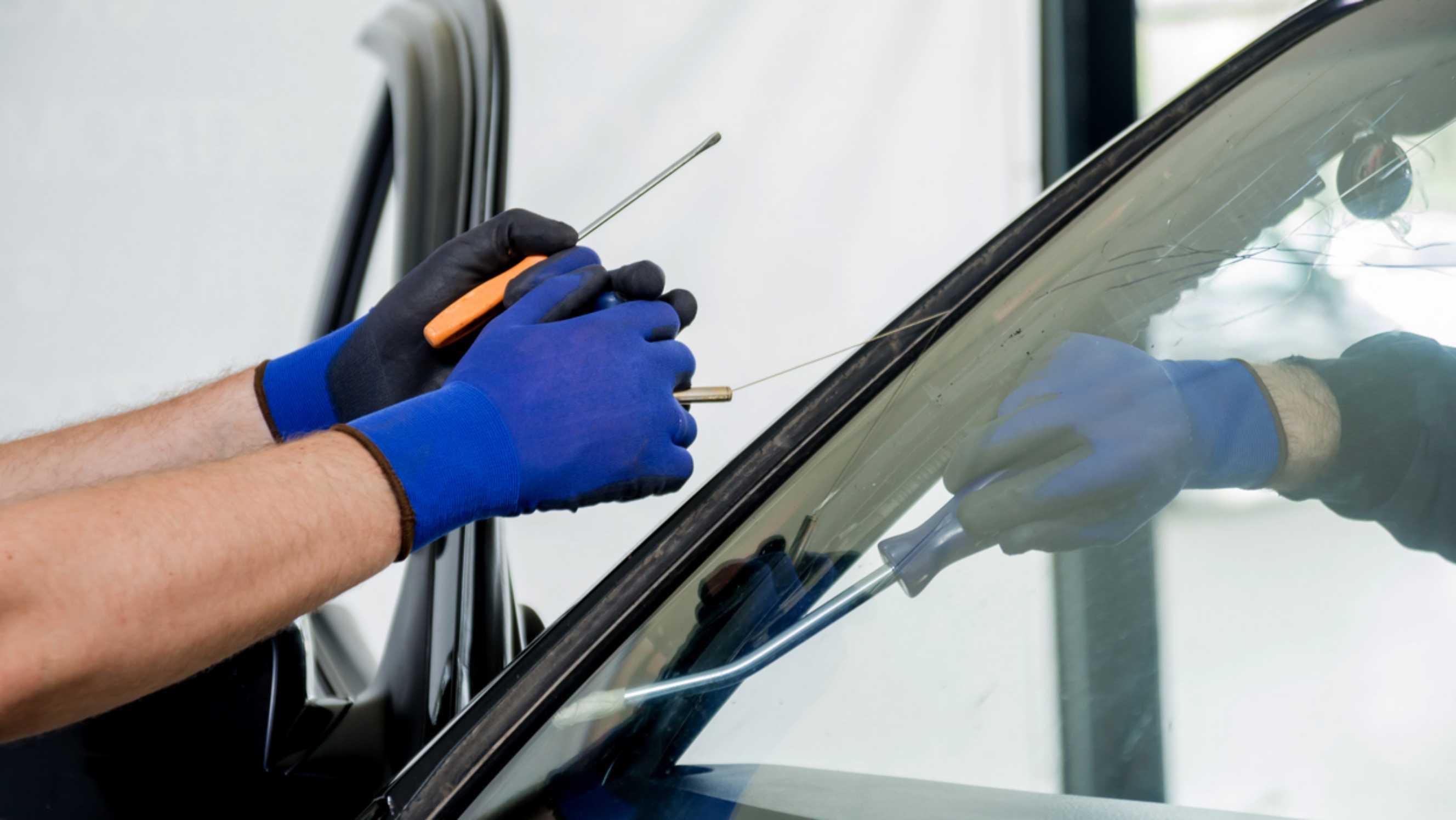 A technician wearing blue gloves using specialised tools to repair a car window, representing efficient car window repair services near you.