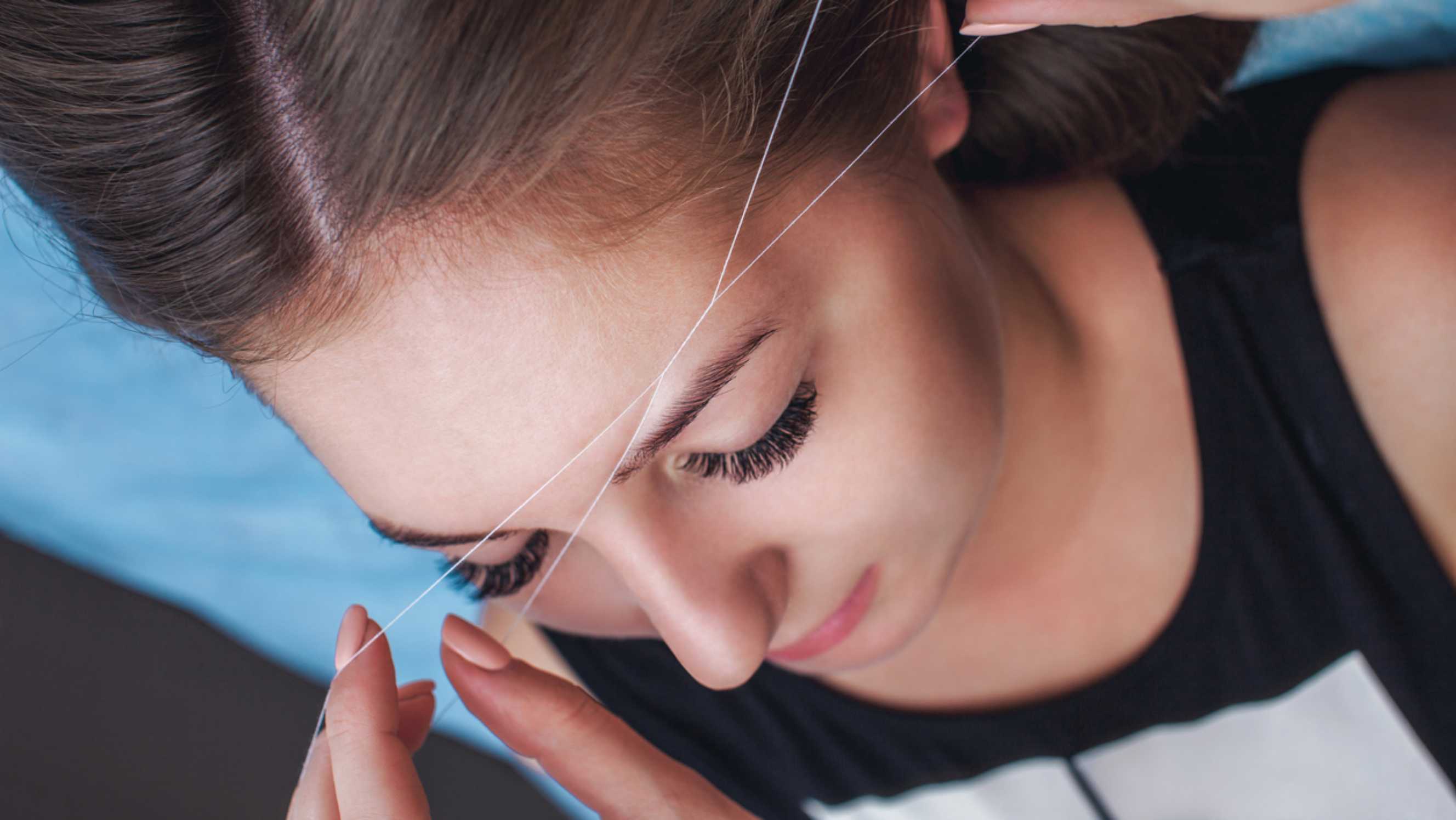 A beautician performing precise eyebrow threading on a client, representing professional eyebrow threading near you.