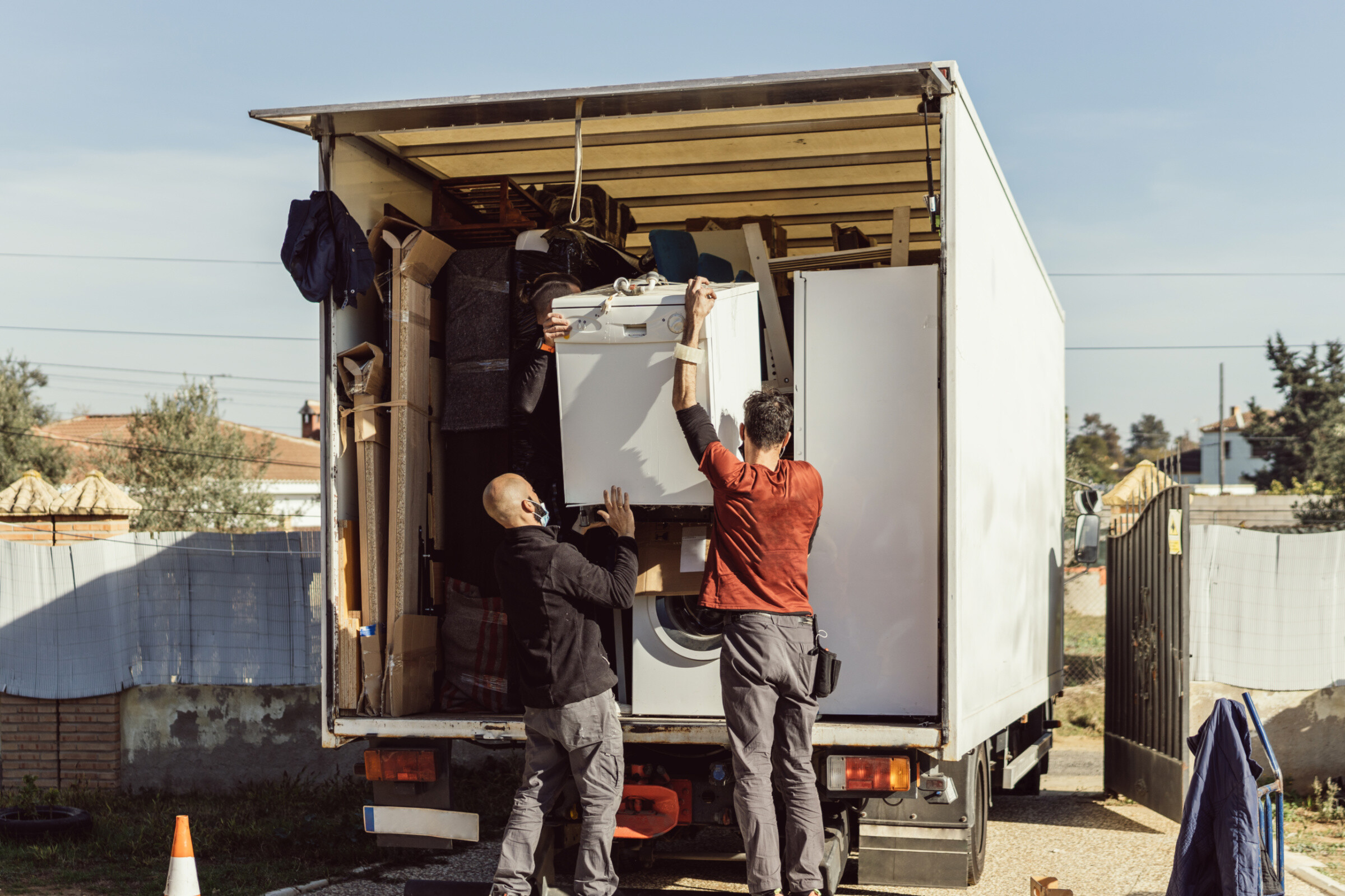 Full shot of 3 colleagues of a moving company load a dishwasher onto the truck