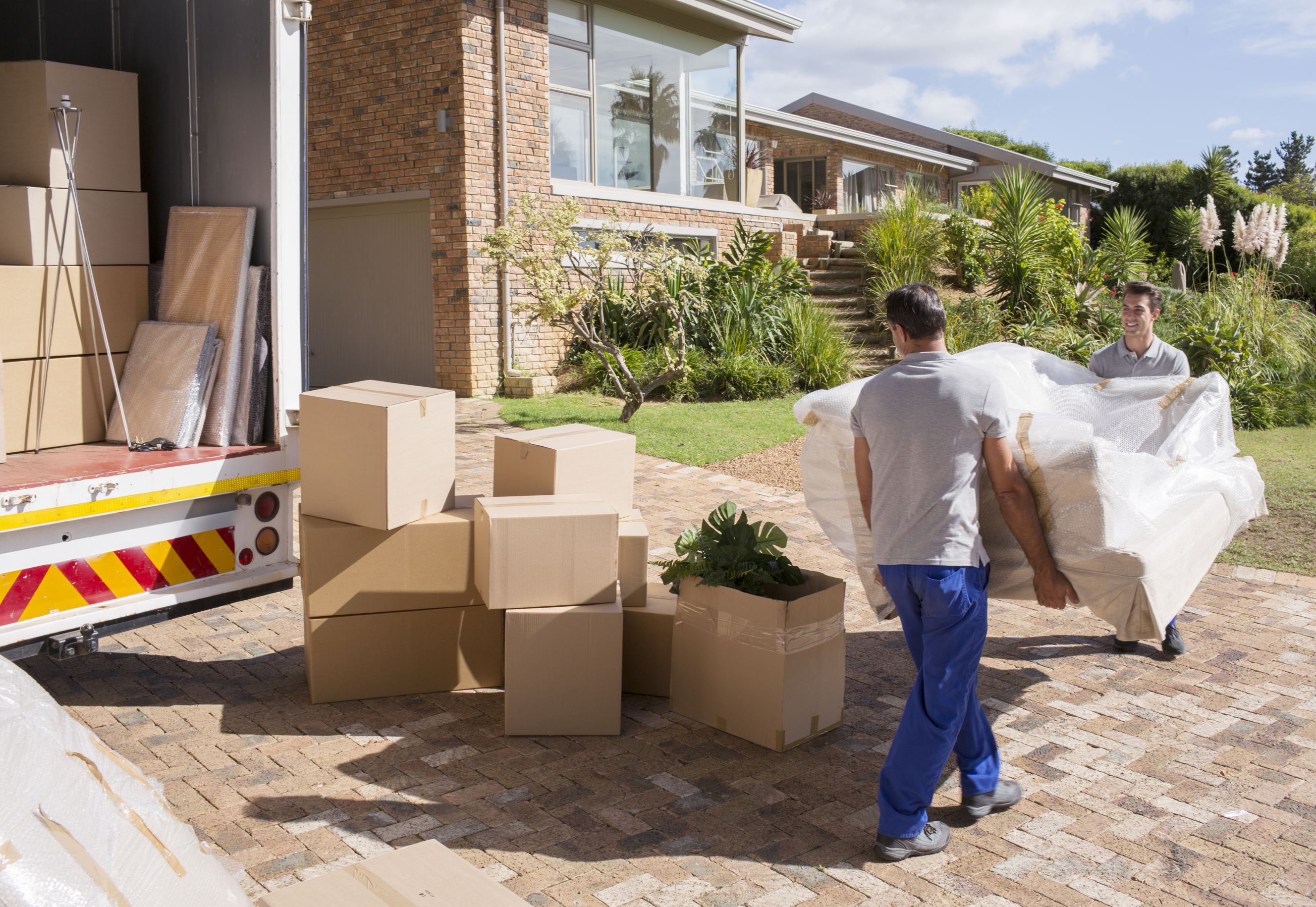 Short distance movers carrying sofa from moving van to house.