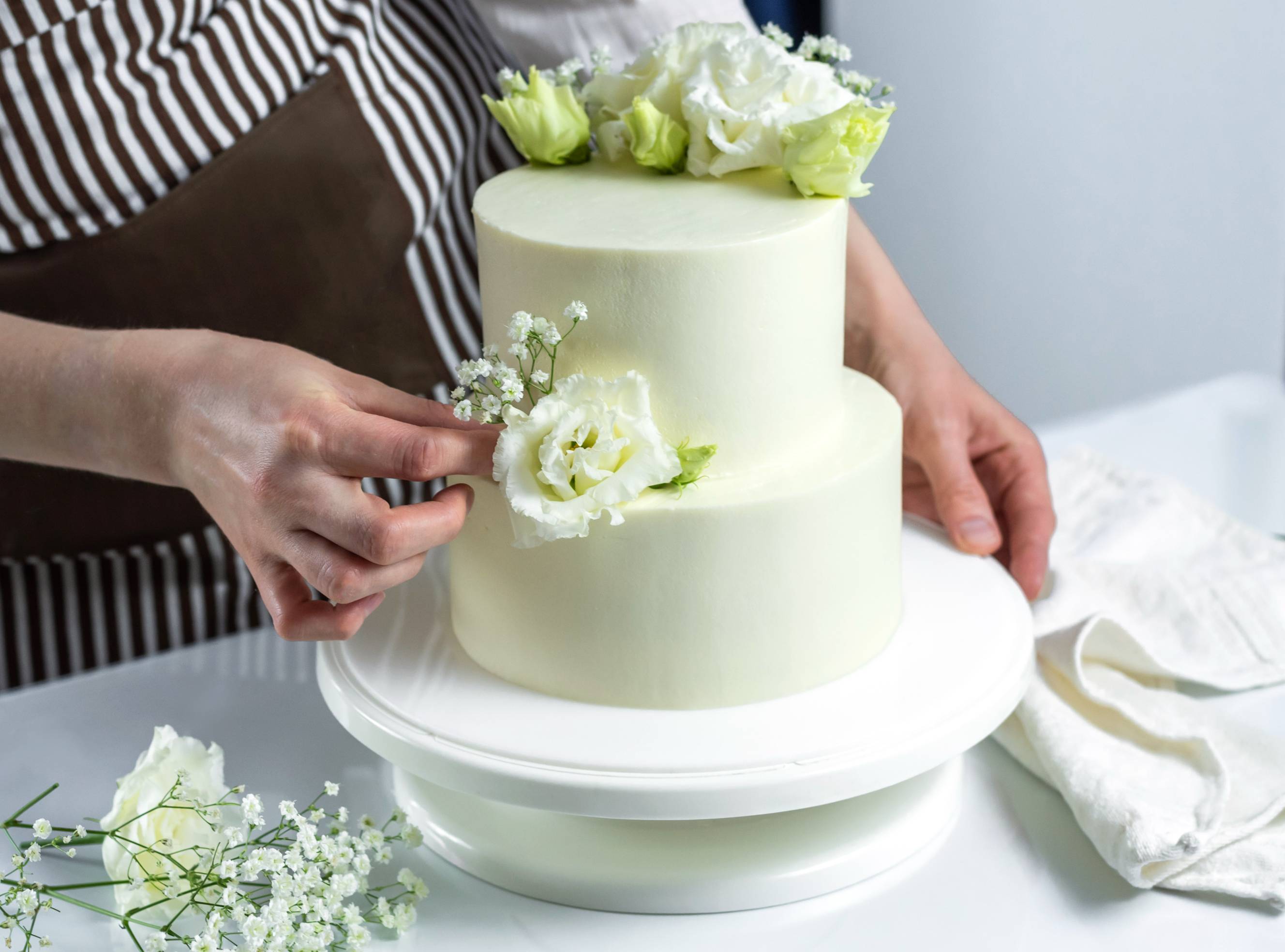 A wedding cake baker near me decorating a white cake with flowers