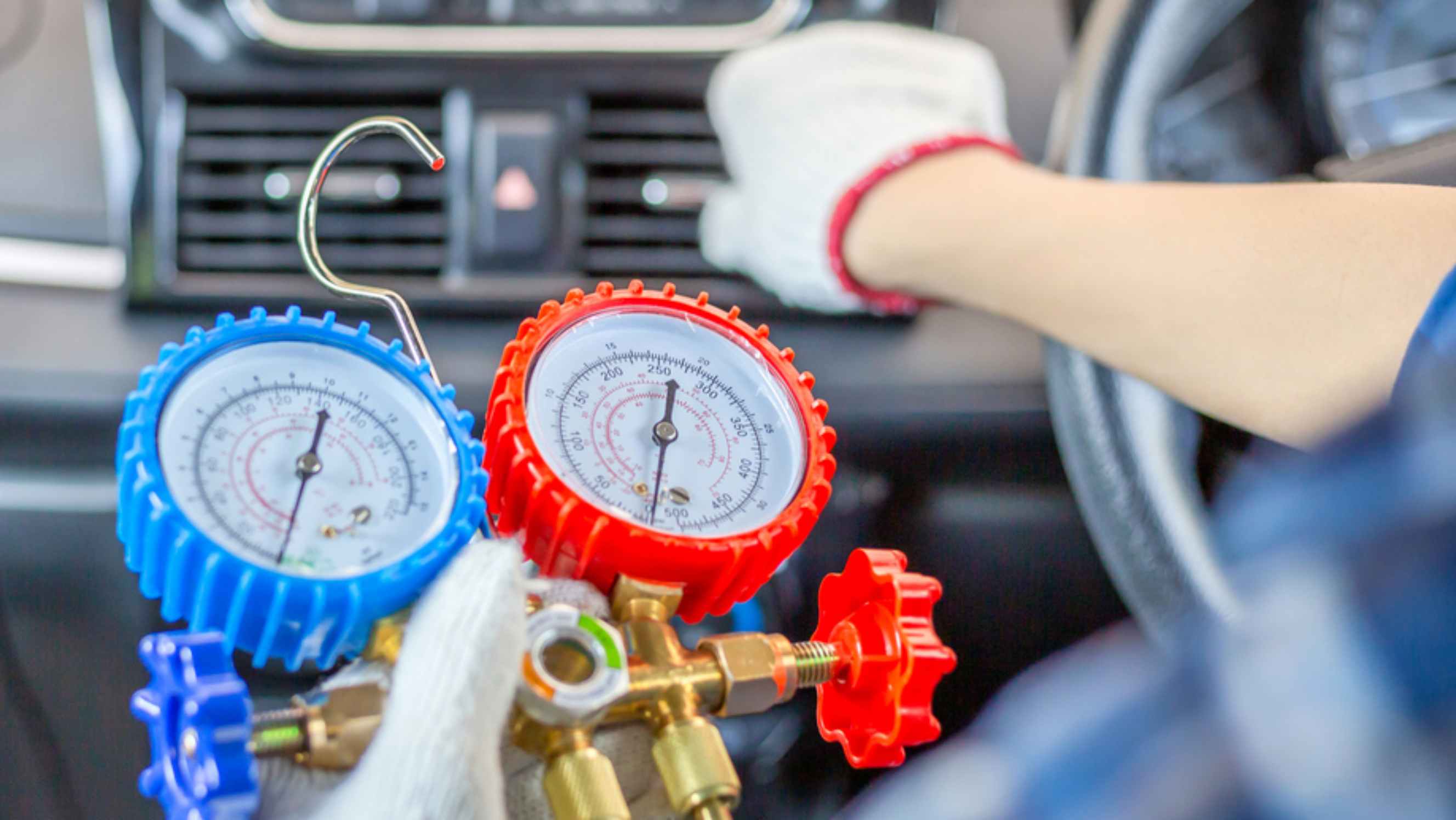 A technician performing a mobile car air conditioning service near you, using gauges to measure pressure while inspecting the car's air conditioning system. 