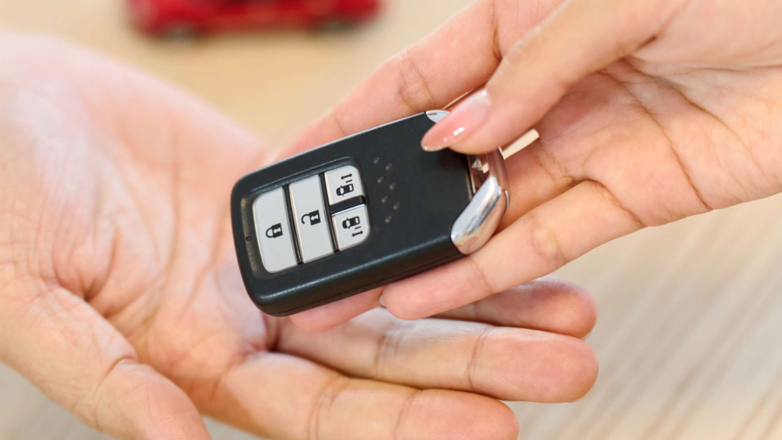 The key fob is being passed from one hand to another, and the background features a subtle focus, indicating a car key repair or replacement service near you.