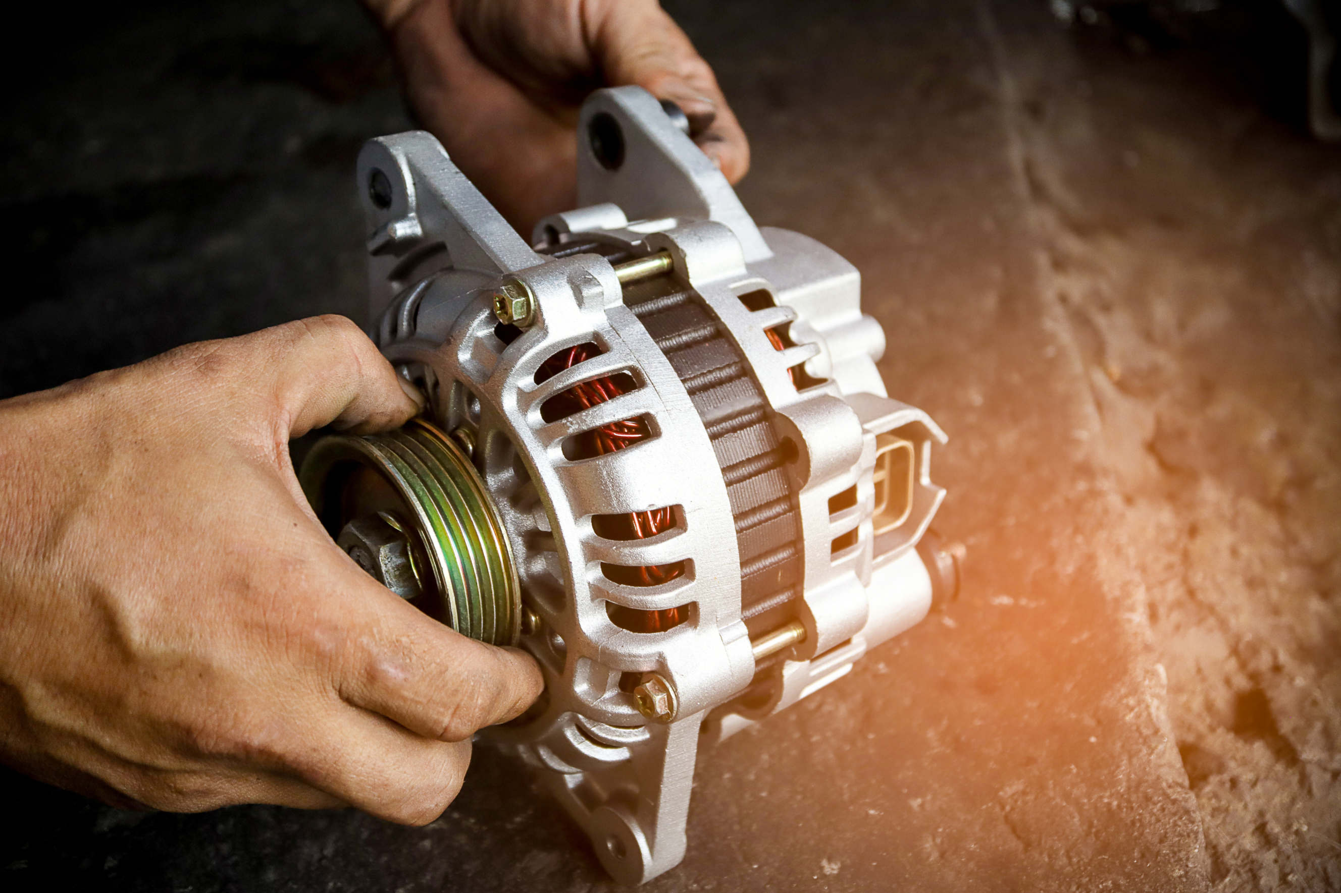 Mechanic holding a car alternator during the replacement process.