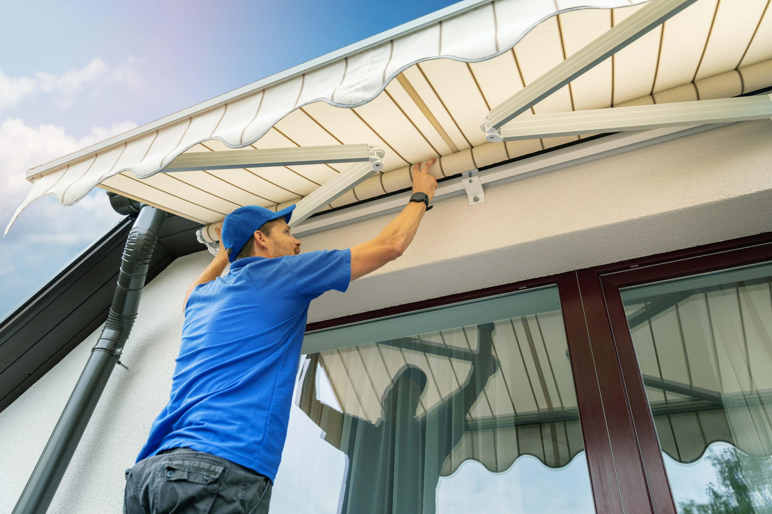 A professional in a blue uniform secures a retractable awning to a home's exterior.