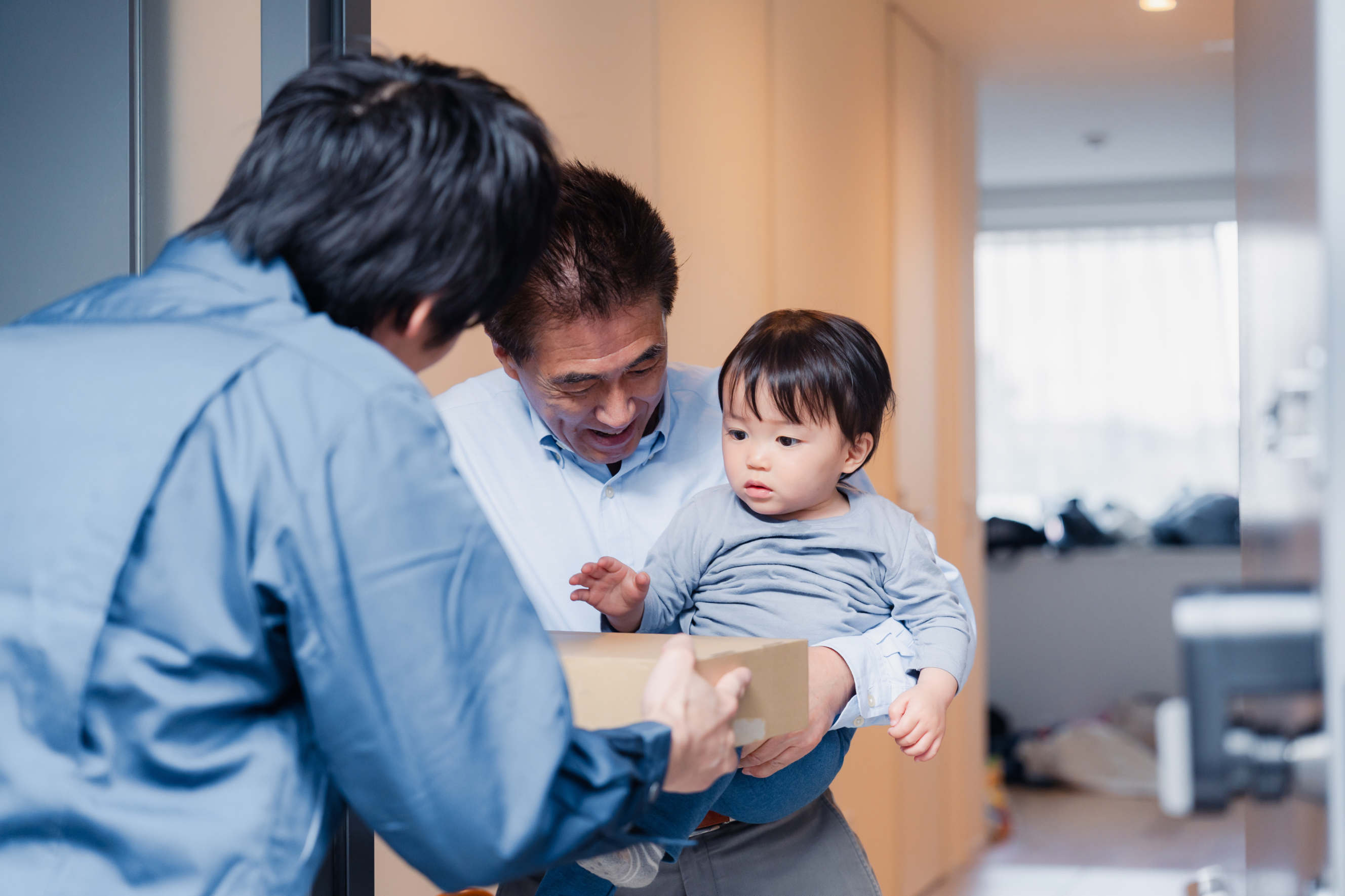 A grandfather holding his grandchild receives a package from a delivery worker at the door.