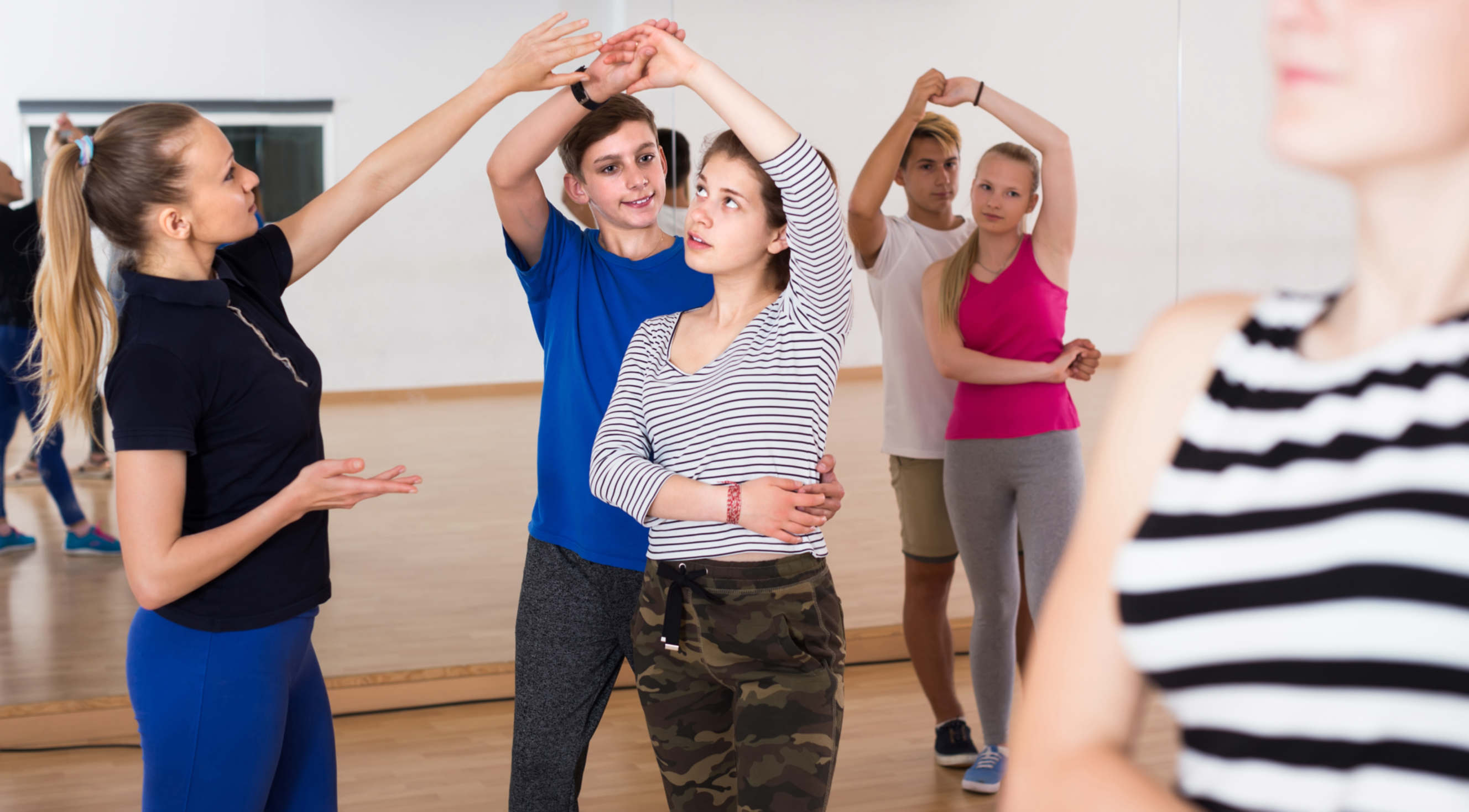 Young couples learning ballroom dance in a studio with an instructor guiding them.