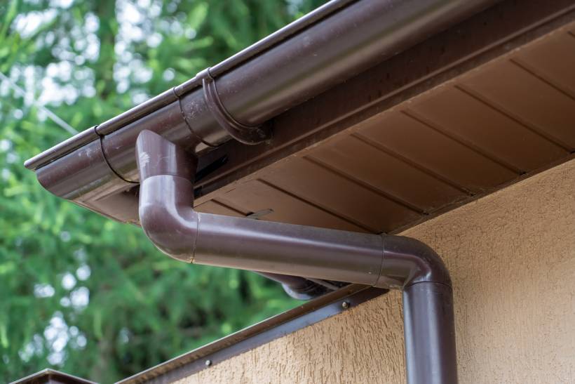 gutter cleaning cost - a brown plastic gutter system against trees