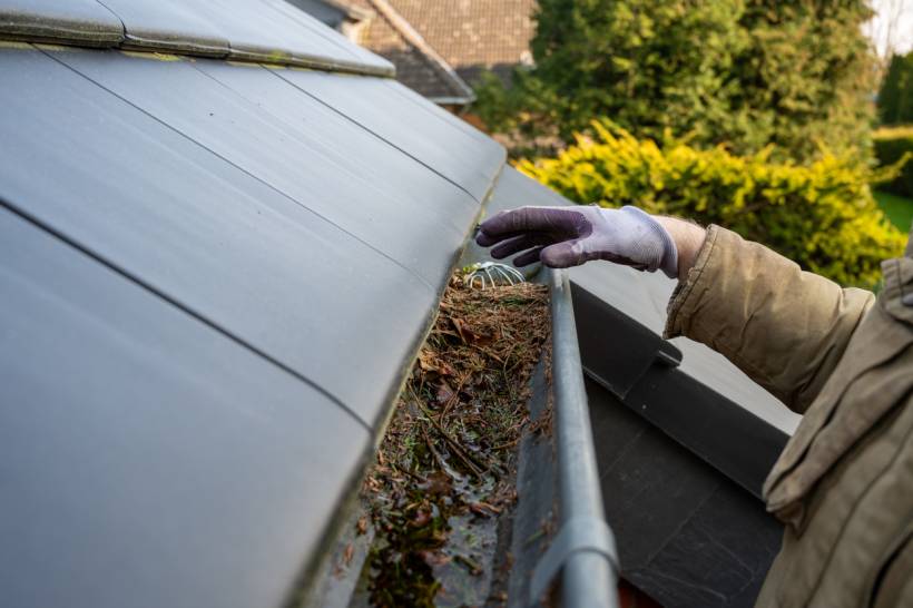 gutter cleaning cost - a man cleaning a blocked rain gutter