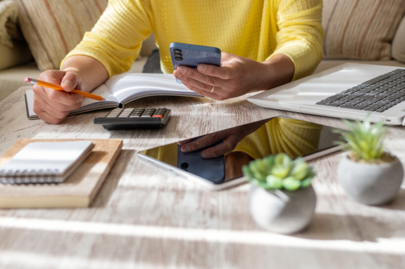 how much do tattoos cost - Woman using a calculator and smartphone to budget her finances, possibly for a tattoo, with notebooks and decor on the table