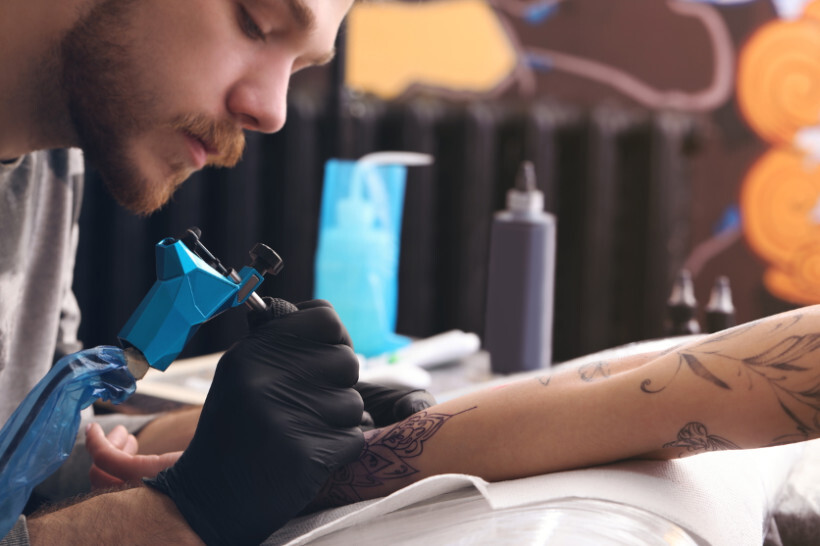 how much do tattoos cost - Close-up of a male tattoo artist carefully inking a black and grey design on a client's arm