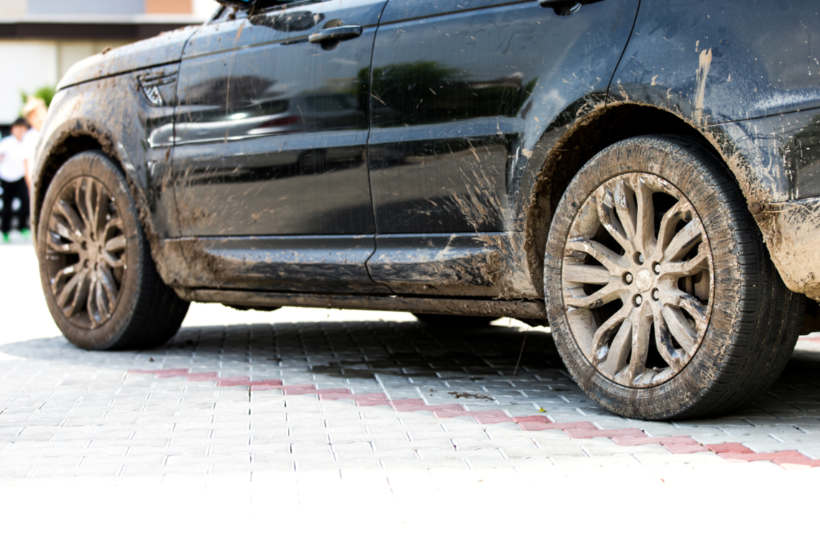 Car wash cost - A black SUV covered in mud, parked on a paved surface.