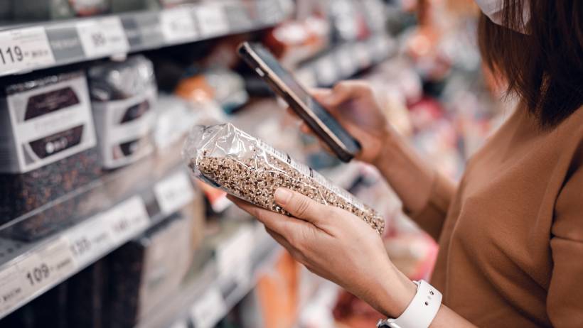 A person in a grocery store aisle looking at a product and using a smartphone - getting paid running errands