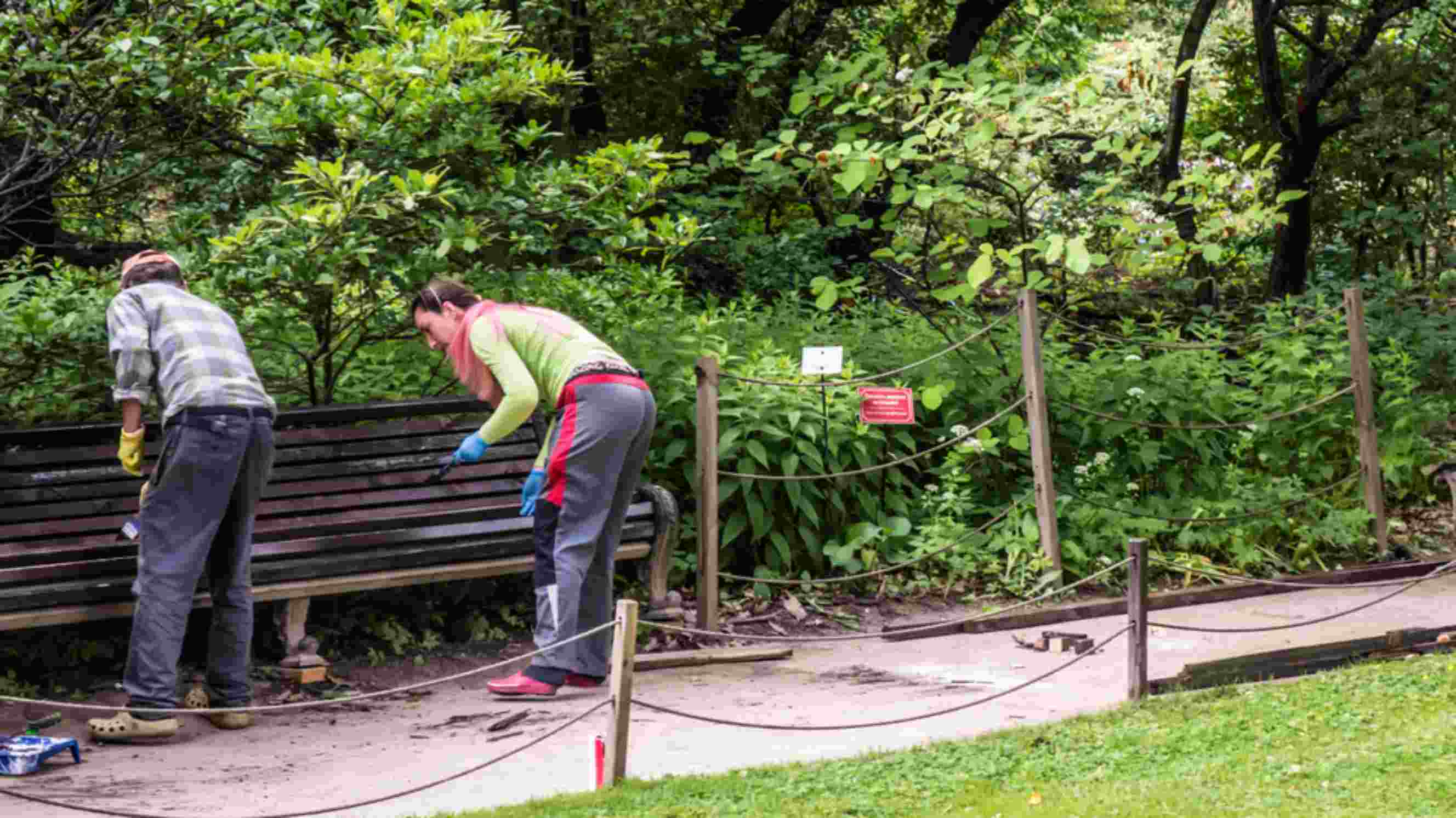 Two people installing and painting a bench in a garden, representing garden bench installations near you