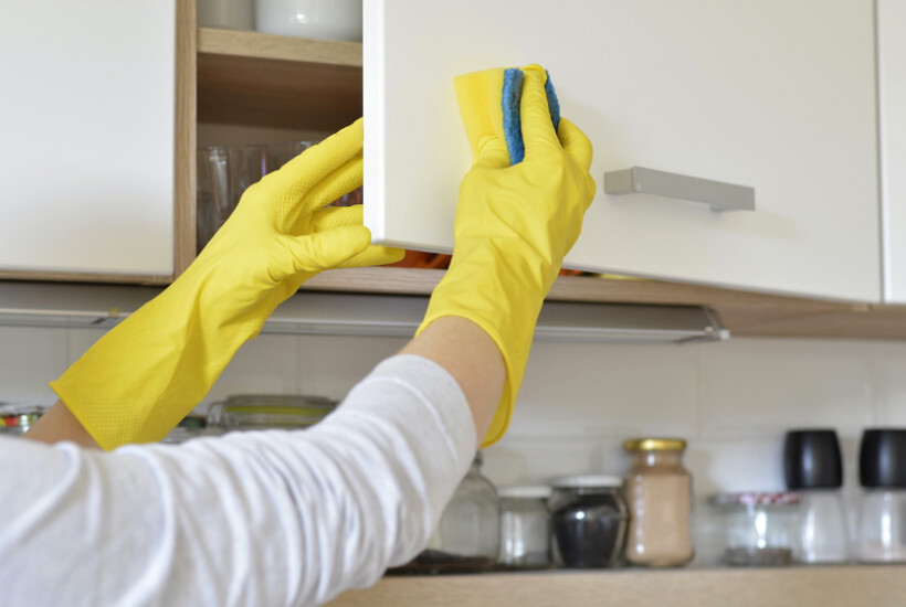 how to eradicate pantry weevils - a person wearing yellow rubber gloves scrubbing a white kitchen cabinet with a sponge