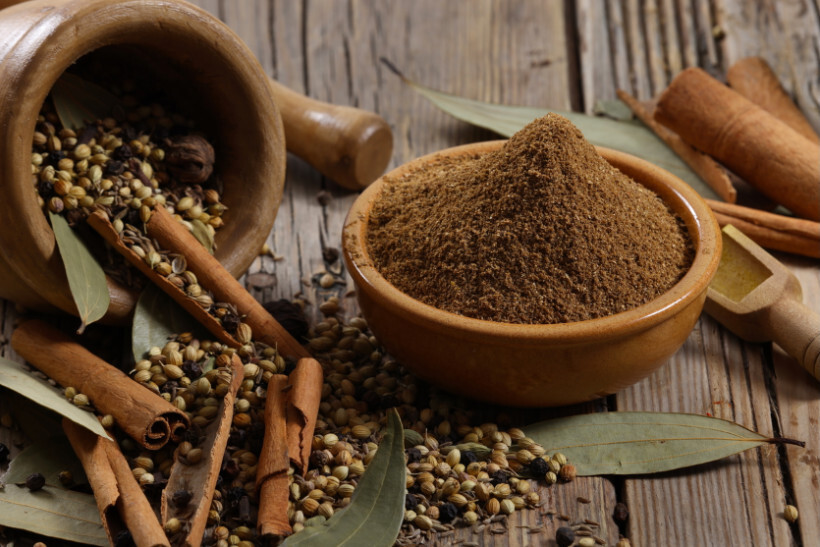 how to eradicate pantry weevils - a bowl of garam masala surrounded by whole spices like cinnamon sticks, bay leaves, and coriander seeds on a wooden surface