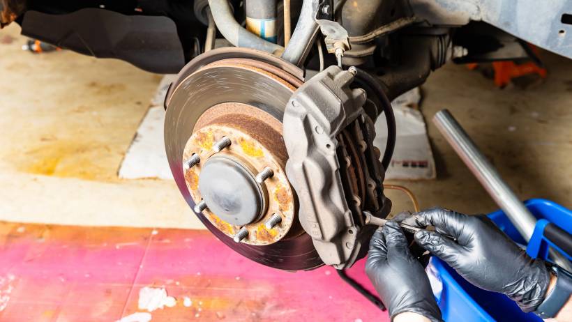 Mechanic wearing black gloves installing brake pads on a rusty disc brake - brake pad replacement cost