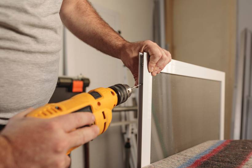 window screen installation - Worker using an electric drill to secure a window screen frame.