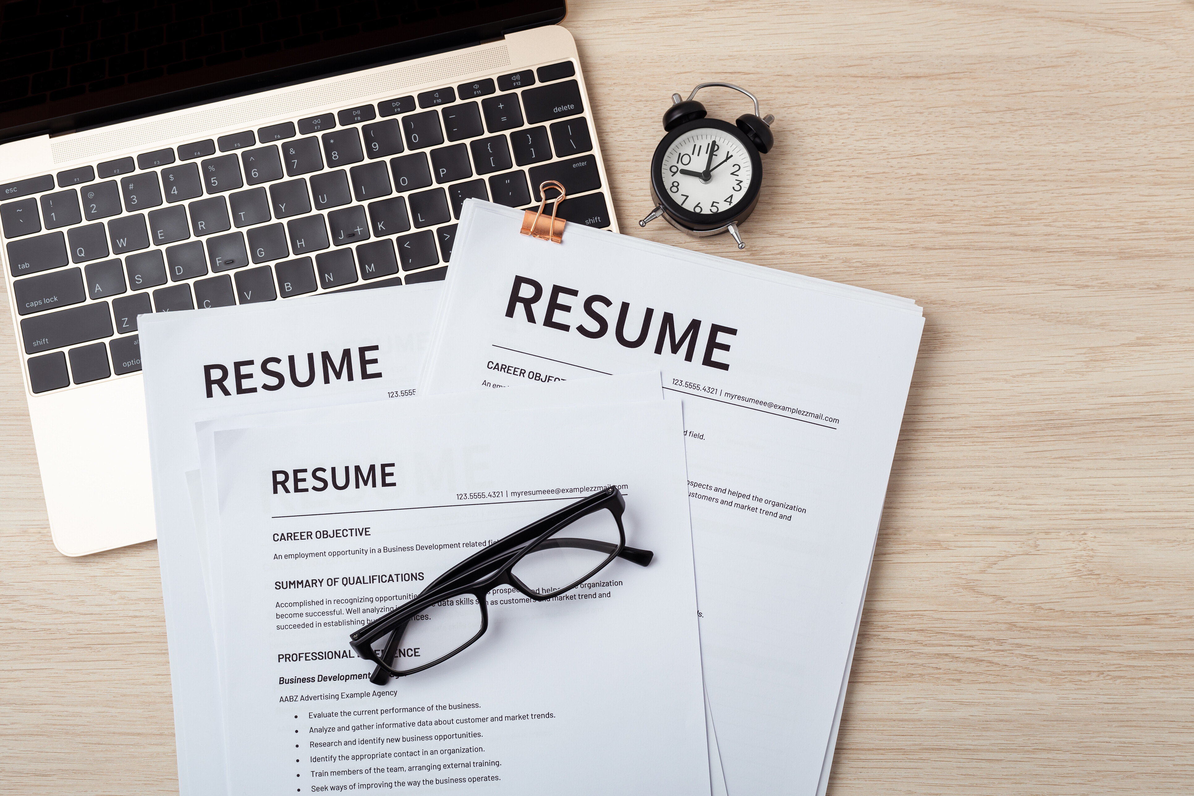How to write a resume – printed resumes on desk with clock and glasses