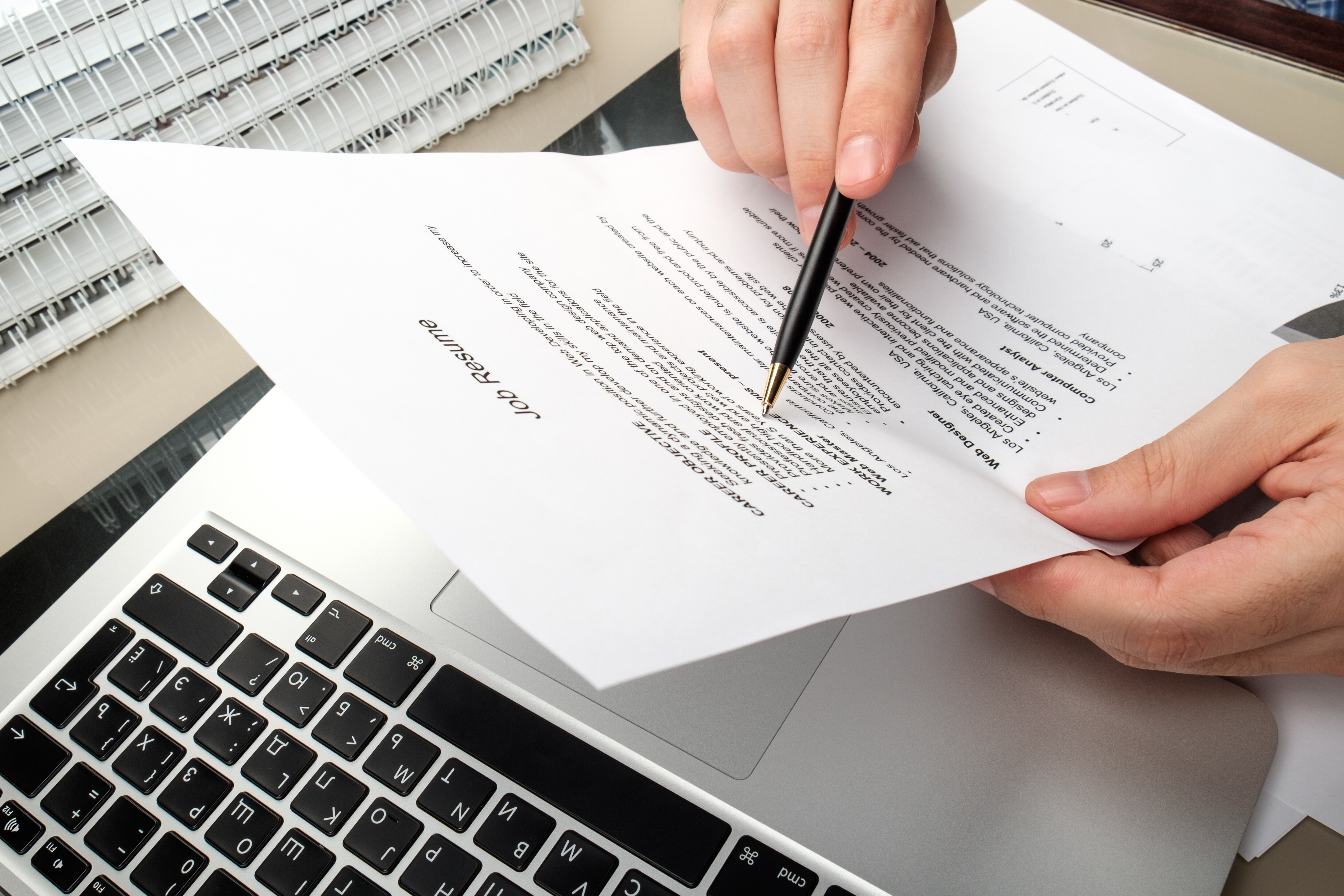How to write a resume – person editing a printed resume over a laptop