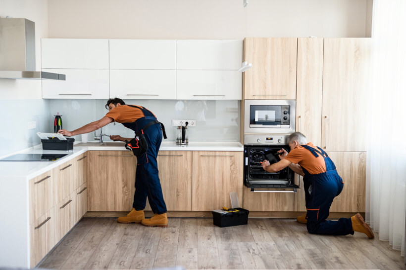 IKEA kitchen cost - Two workers installing sink and oven units in a partially completed kitchen