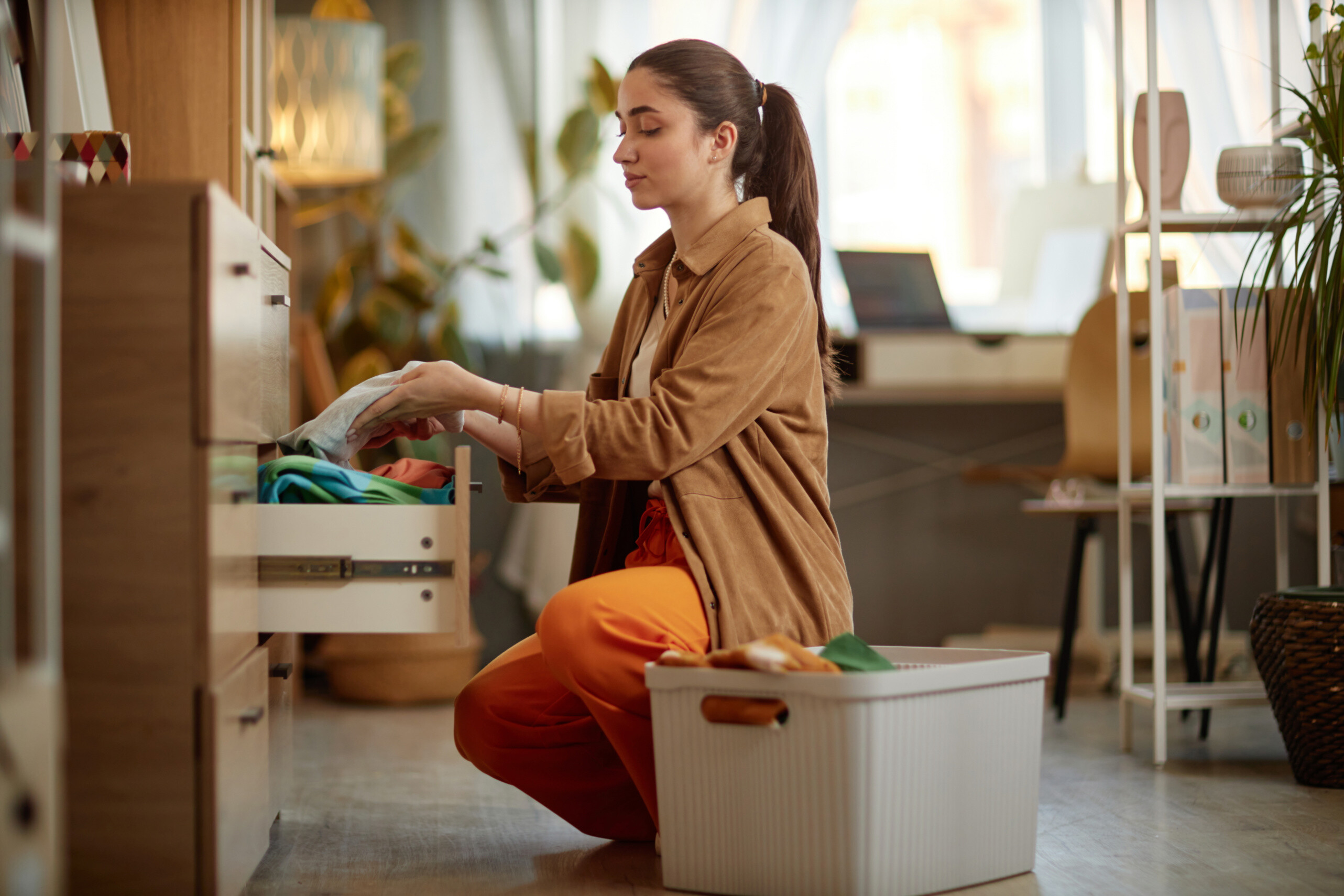 A mother's helper near me is storing clothes in a cabinet.