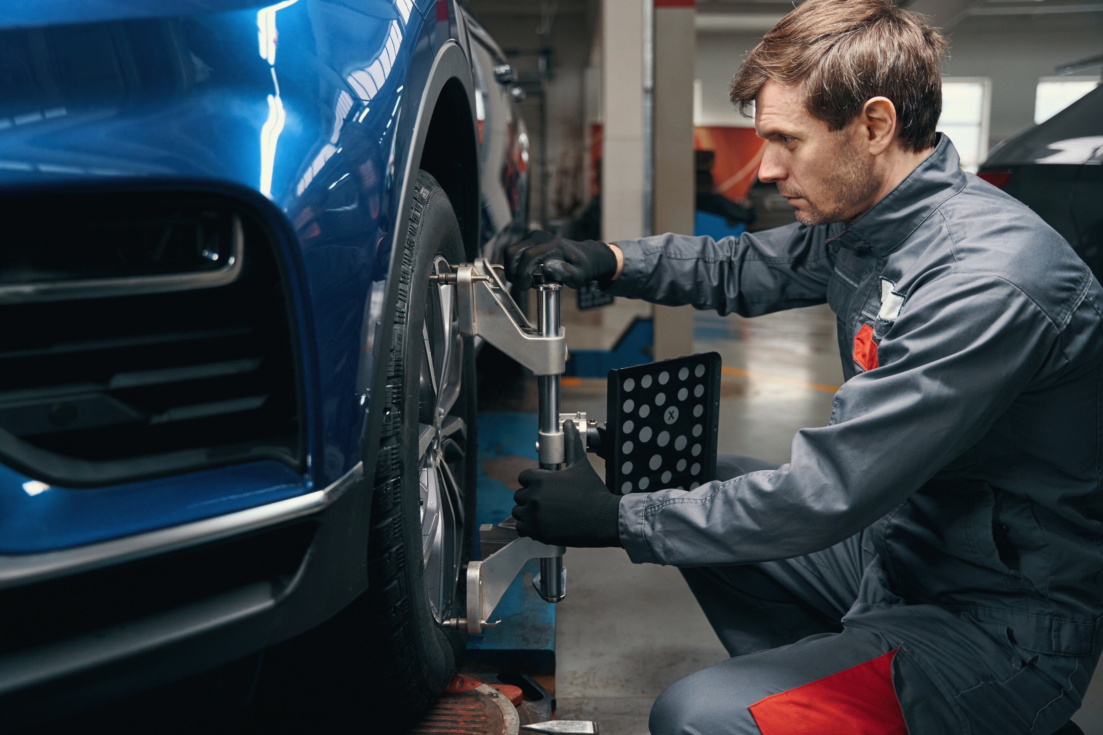 Wheel alignment costs - expert setting camber and toe angle on a blue car