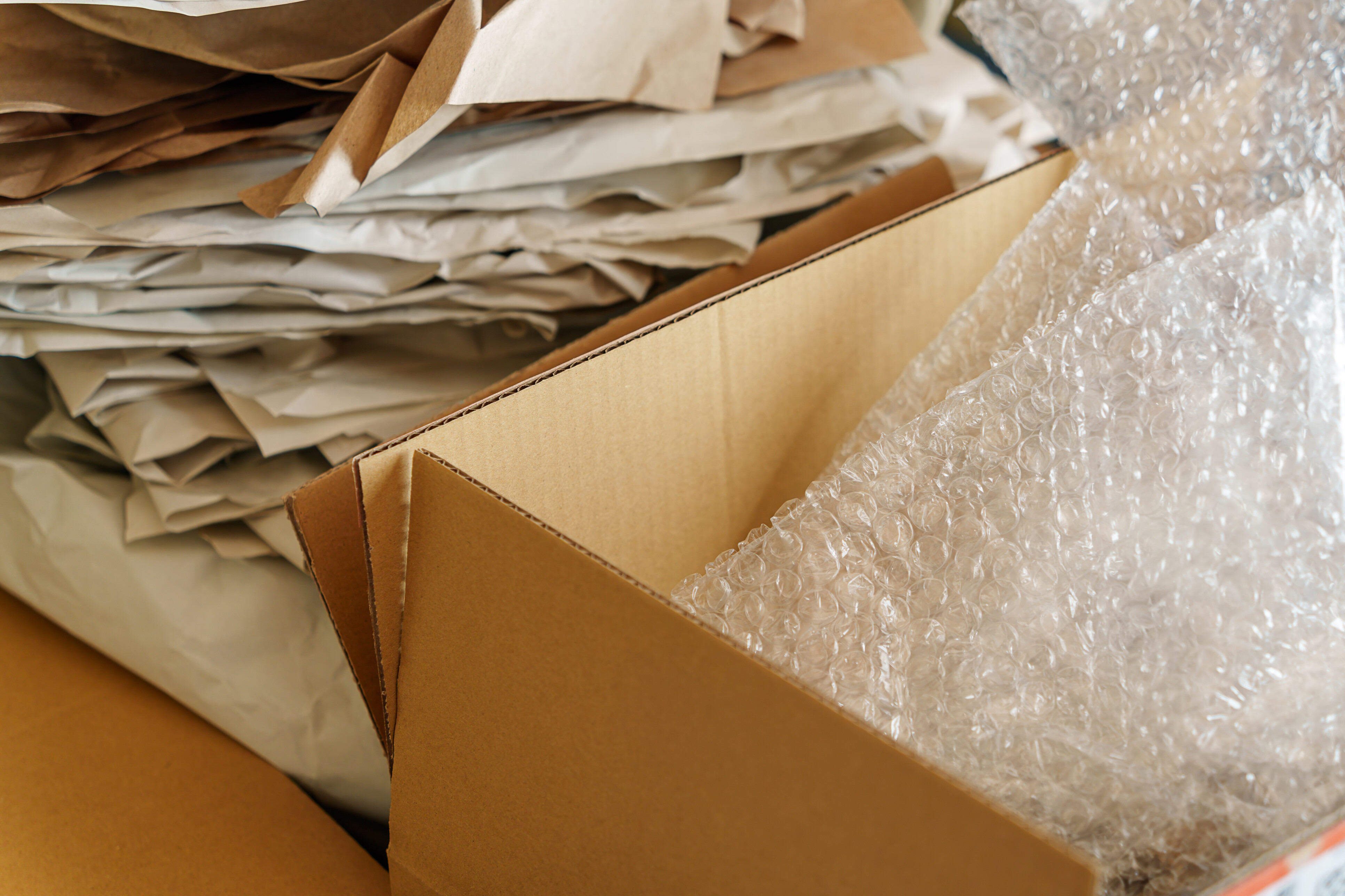 Open cardboard box with bubble wrap and stacked packing paper sheets.