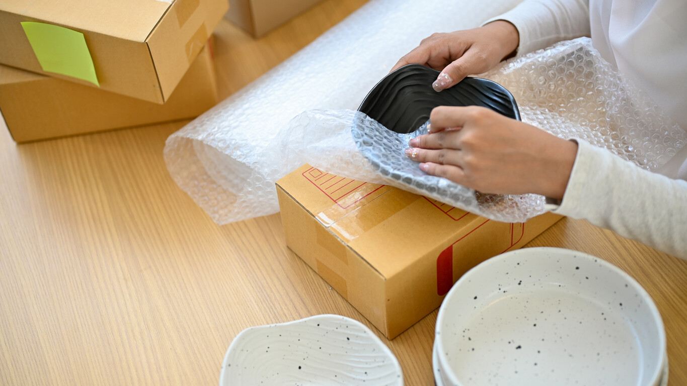 Person wrapping a ceramic bowl in bubble wrap for packaging. - bubble wrap vs packing paper