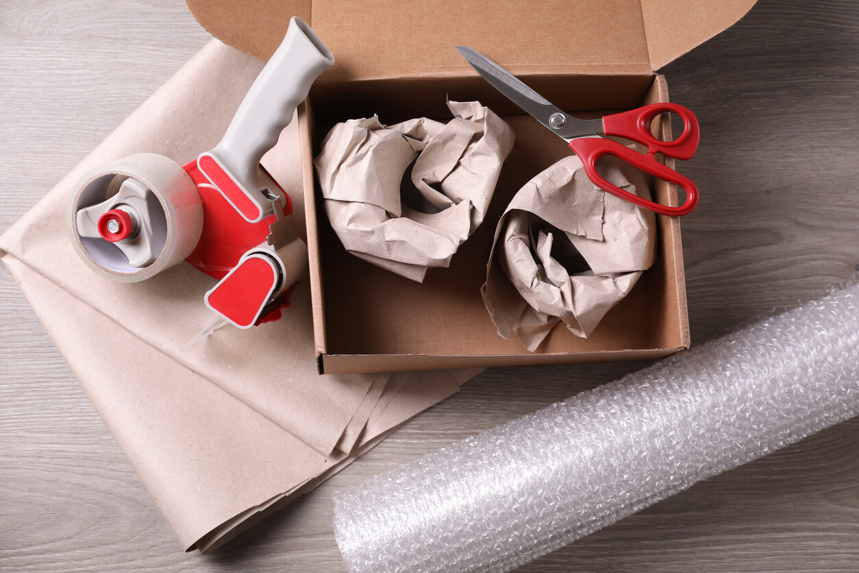 Open box with packing paper, scissors, and tape on a wooden surface. - bubble wrap vs packing paper